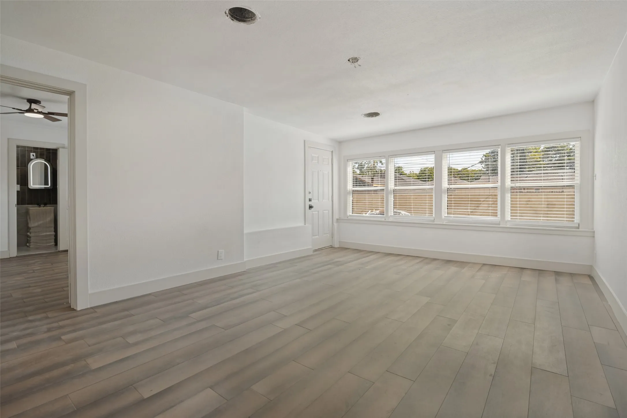 Wood-finish flooring, multiple windows with blinds, recessed lighting, and a white entry door