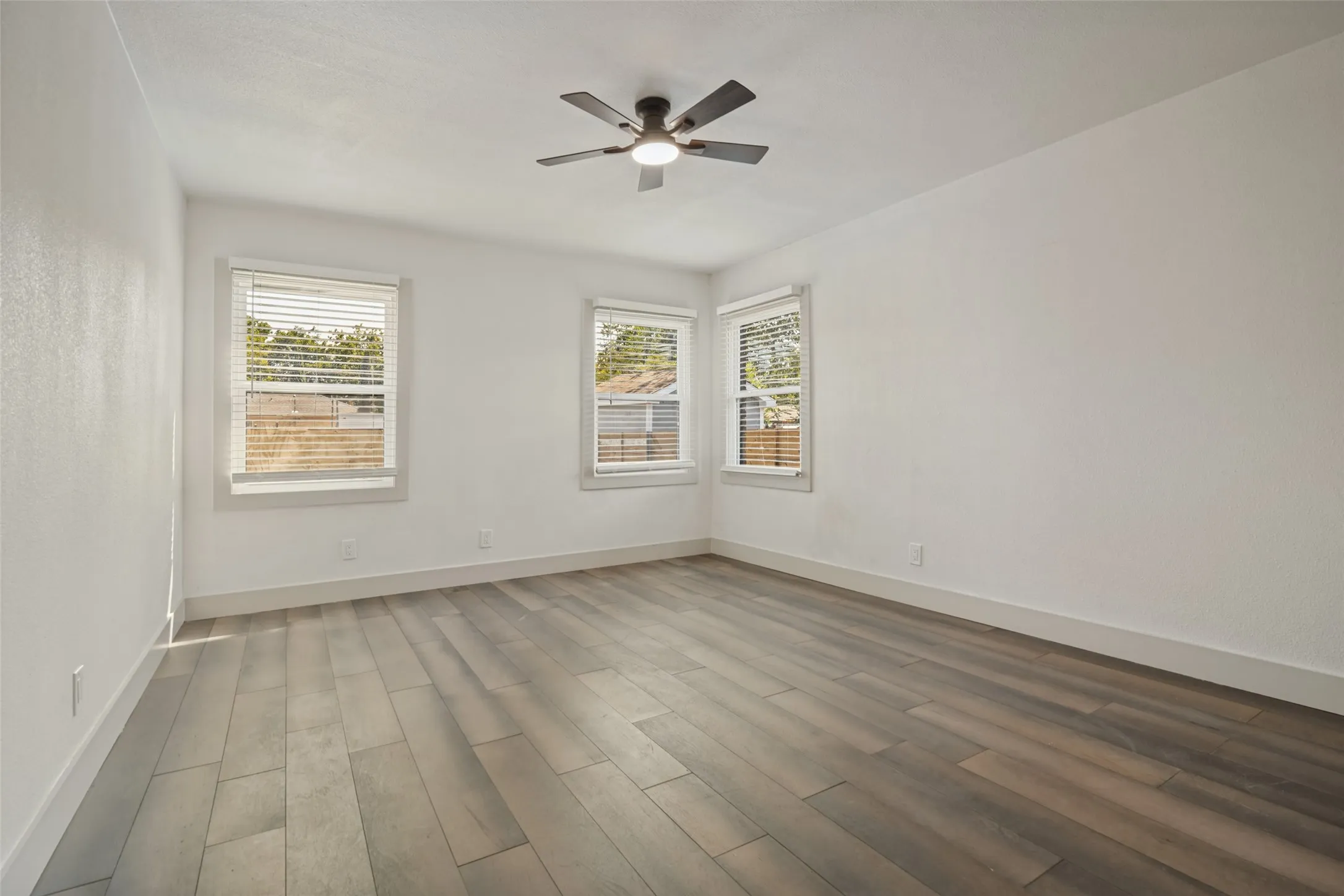Wood-finish flooring with white walls and trim, featuring multiple windows with blinds