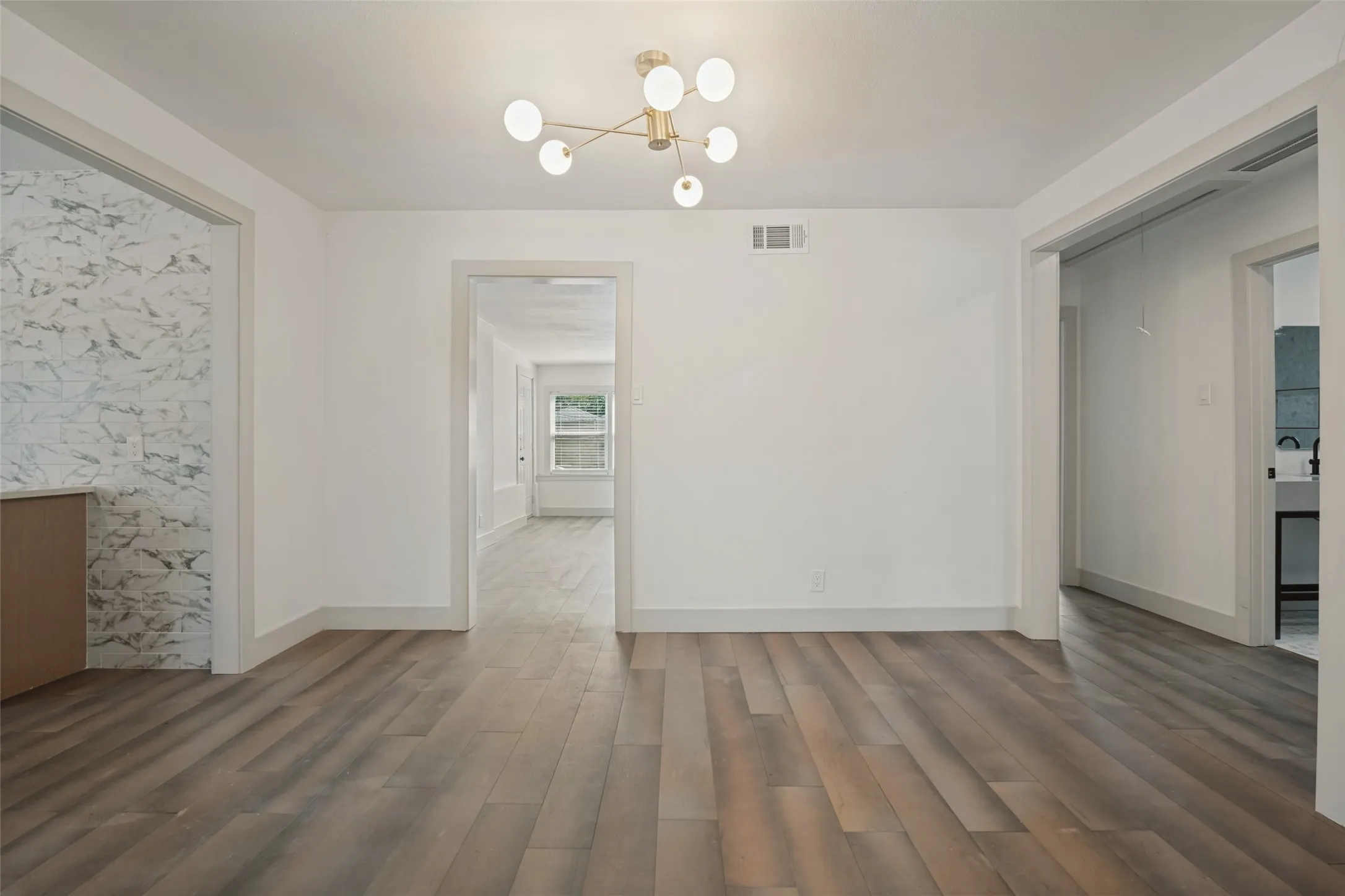 Wood-finish flooring throughout, modern ceiling light fixture, white interior walls, and contrasting wall paneling