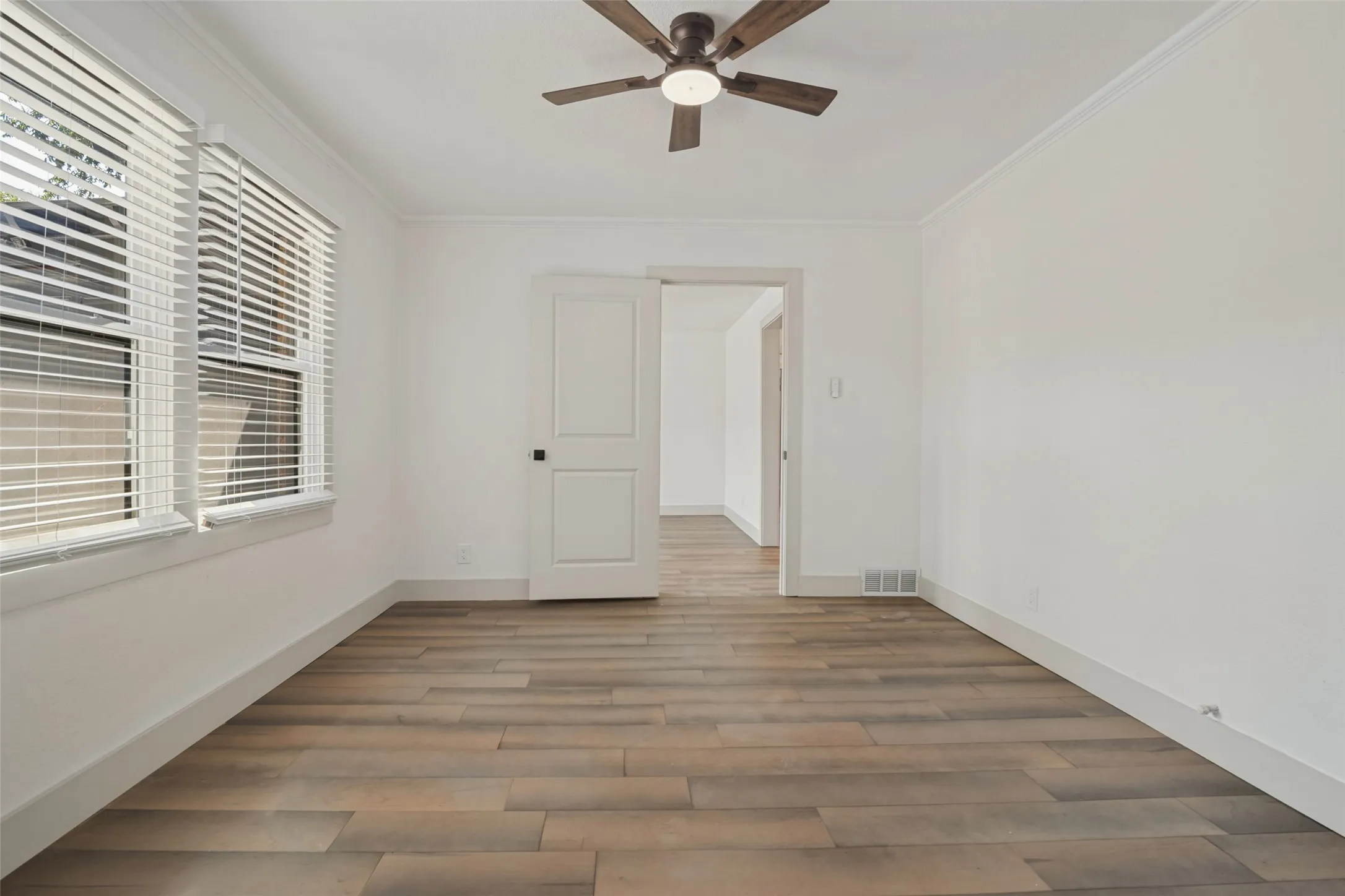 Wood-finish plank flooring, crisp white walls, two paneled doors, and an overhead ceiling fan with integrated lighting