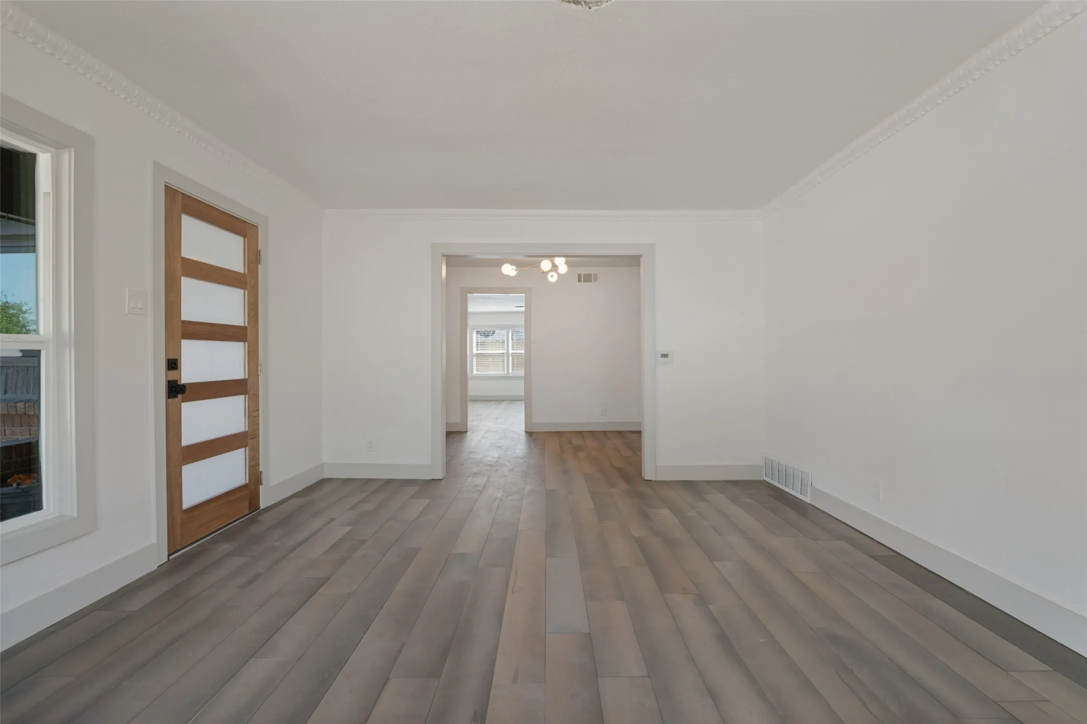 Wood-finish flooring throughout, white painted walls, crown molding, a modern wooden door with frosted glass panels, and an arched entryway