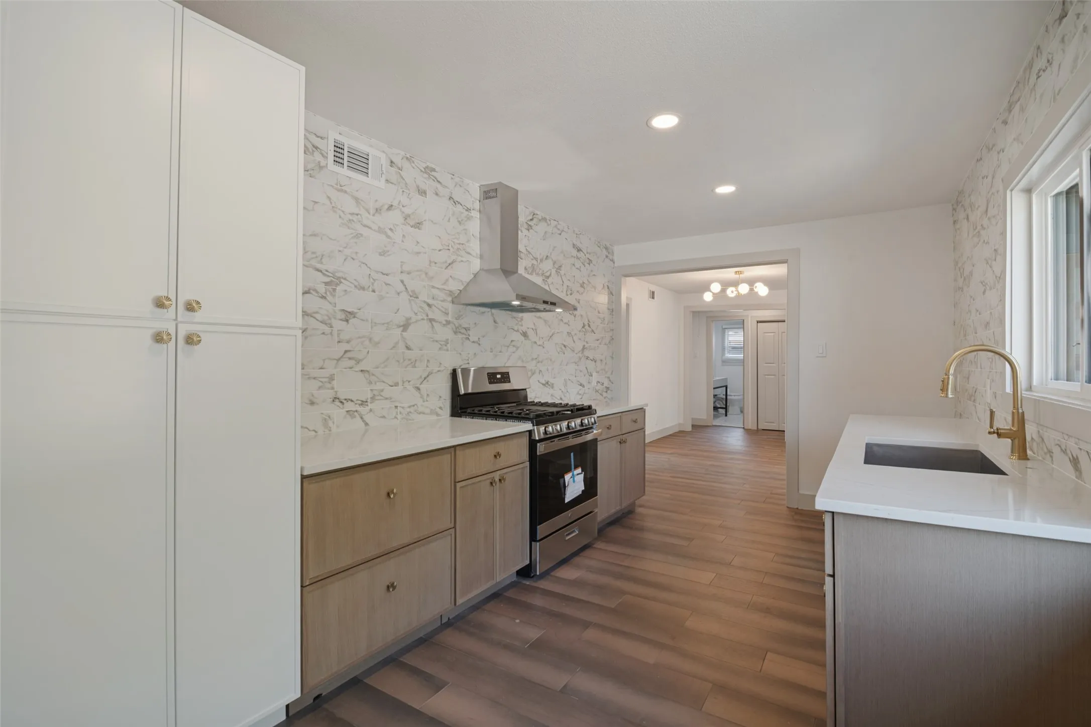 Kitchen featuring white and wood-finish cabinetry, stainless steel range with matching vent hood, white countertops, and wood-finish flooring