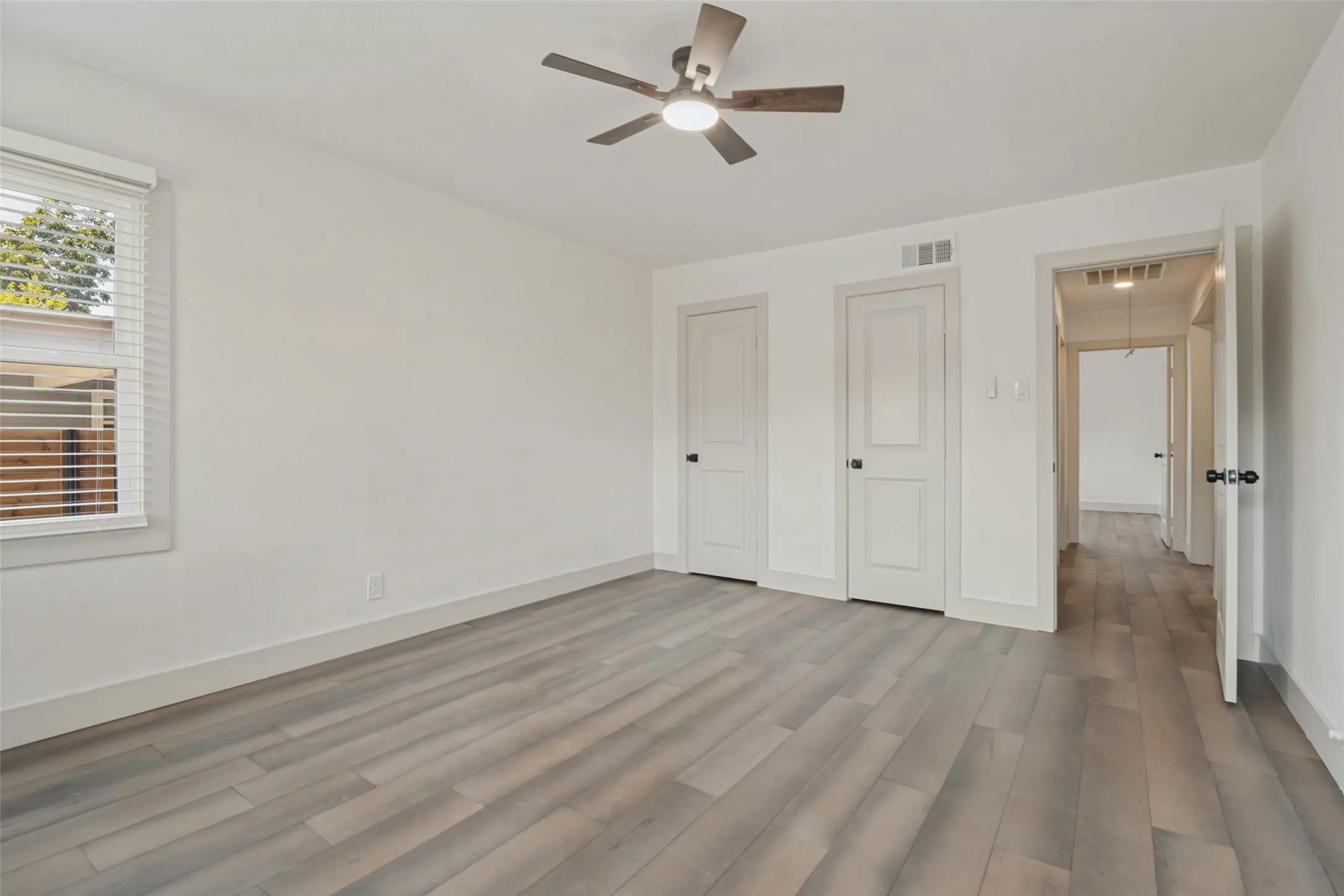 Wood-finish flooring throughout, bright white walls, and a contemporary ceiling fan with integrated lighting