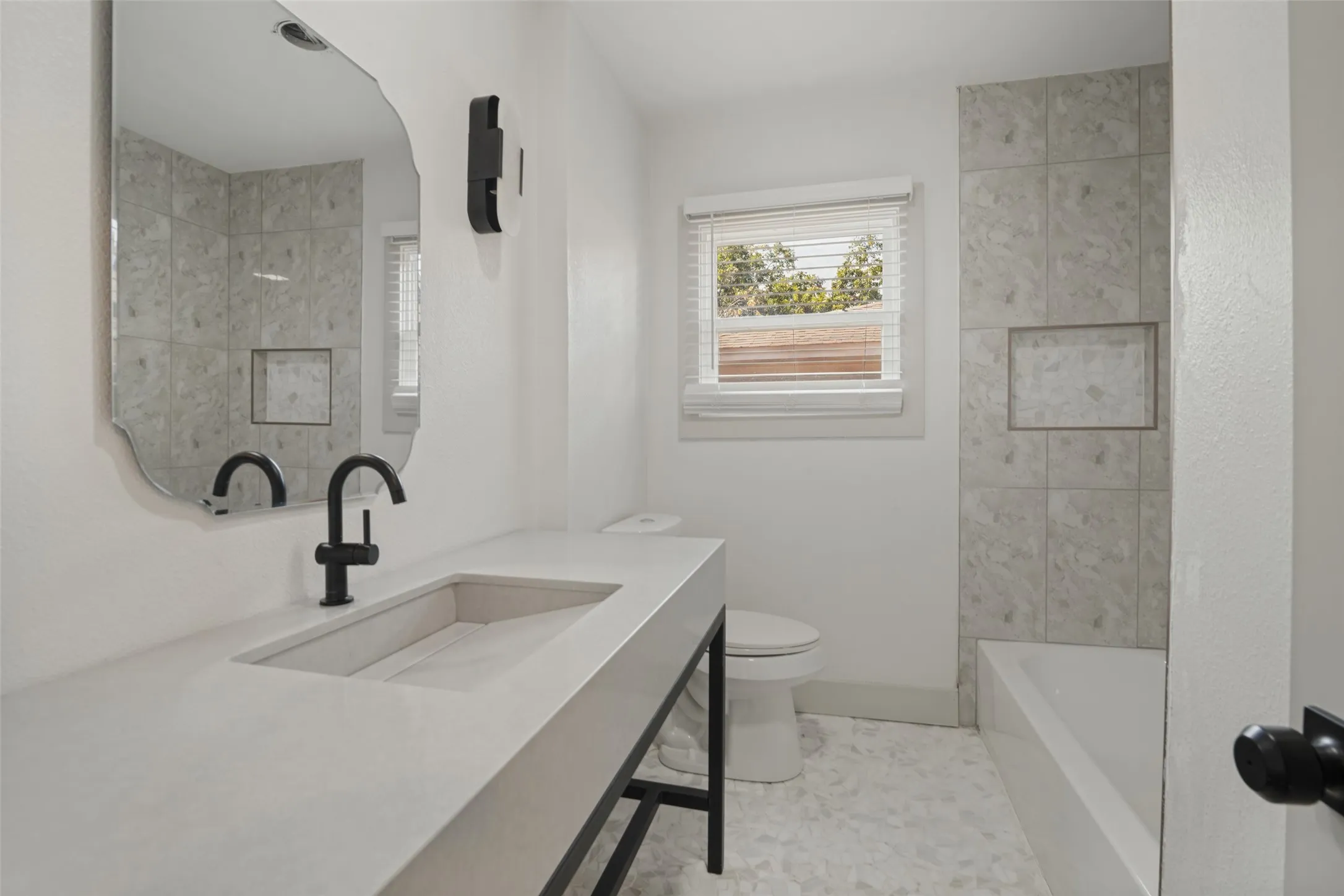 Integrated vanity with built-in sink, matte black faucet, and an ornate frameless mirror