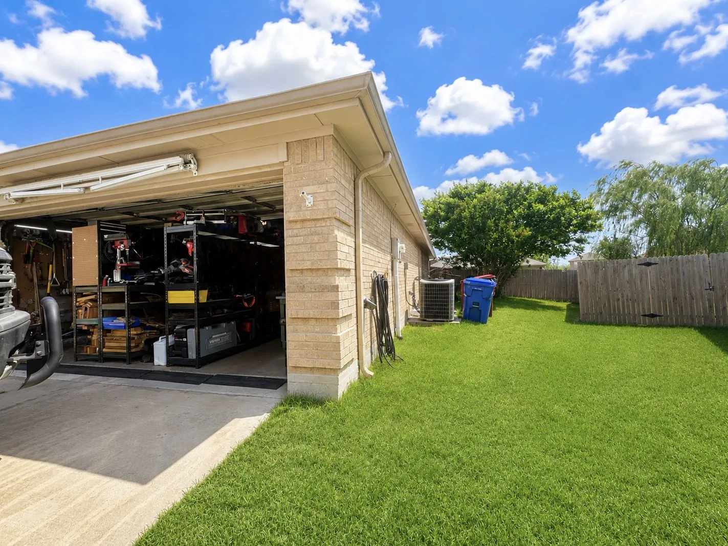 Brick exterior, concrete driveway, lush green lawn, mature trees, wooden privacy fence