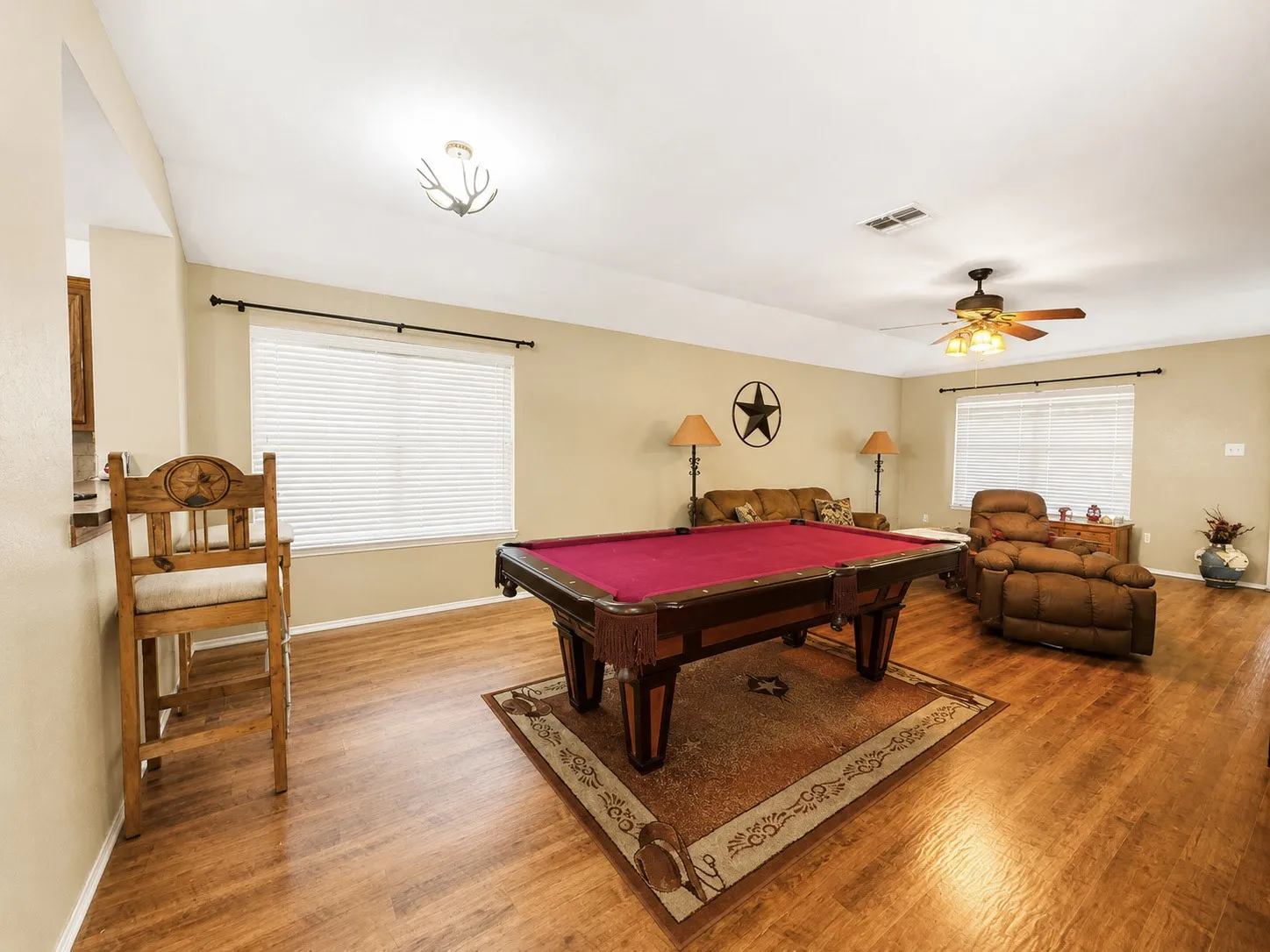 Wood-finish flooring throughout, ceiling fan with integrated lighting, and multiple windows with blinds