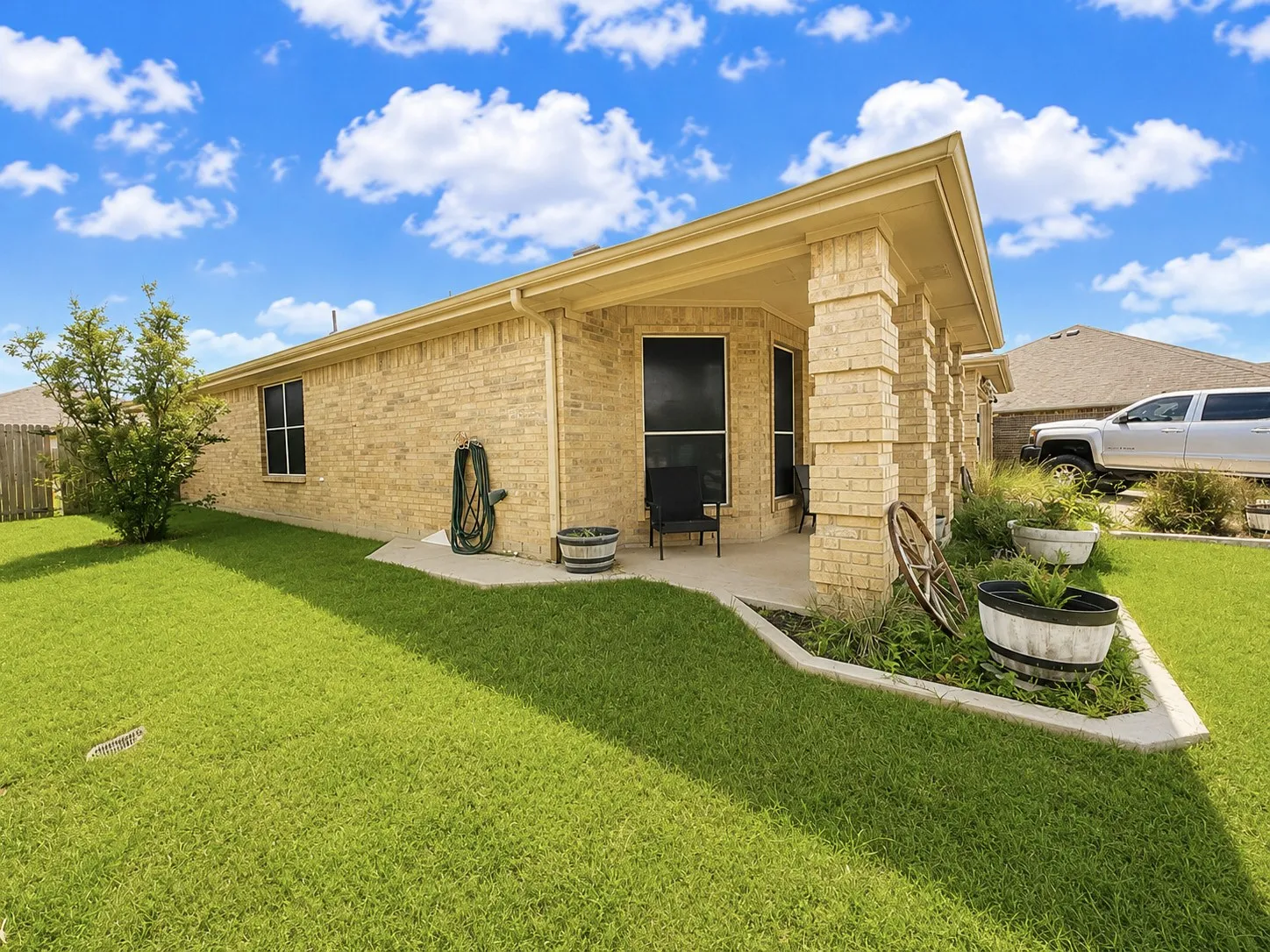 Rear exterior featuring a covered patio, brick columns, and a landscaped bed