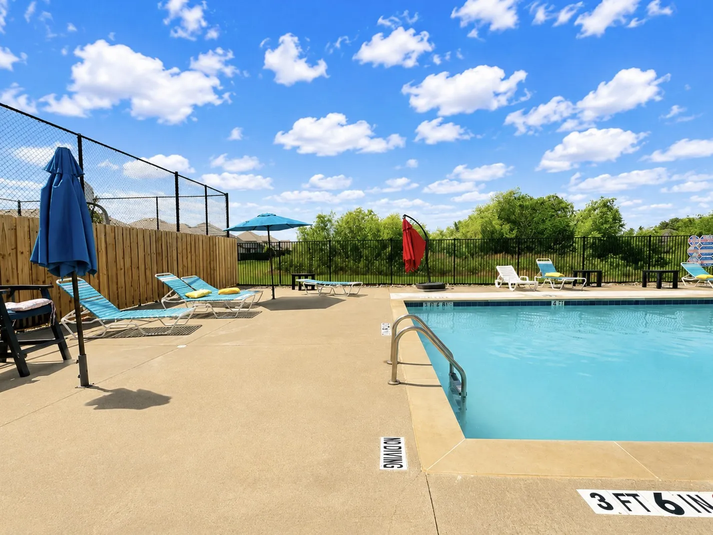 Outdoor swimming pool with a concrete surround, metal pool ladder, and chain-link fencing