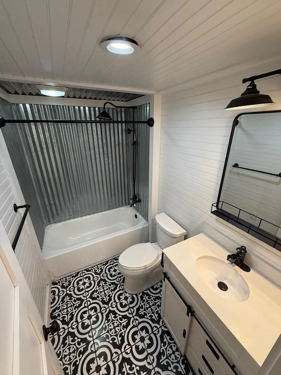 Bathroom with patterned floor tile, corrugated metal shower surround, white vanity with integrated sink, and white shiplap walls