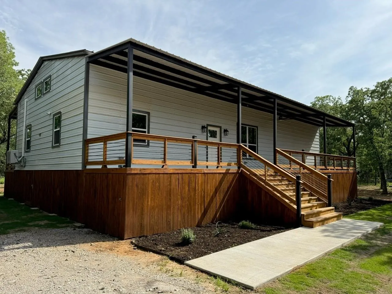 Expansive covered porch featuring a wood deck, wood railing with cable infill, and a concrete pathway