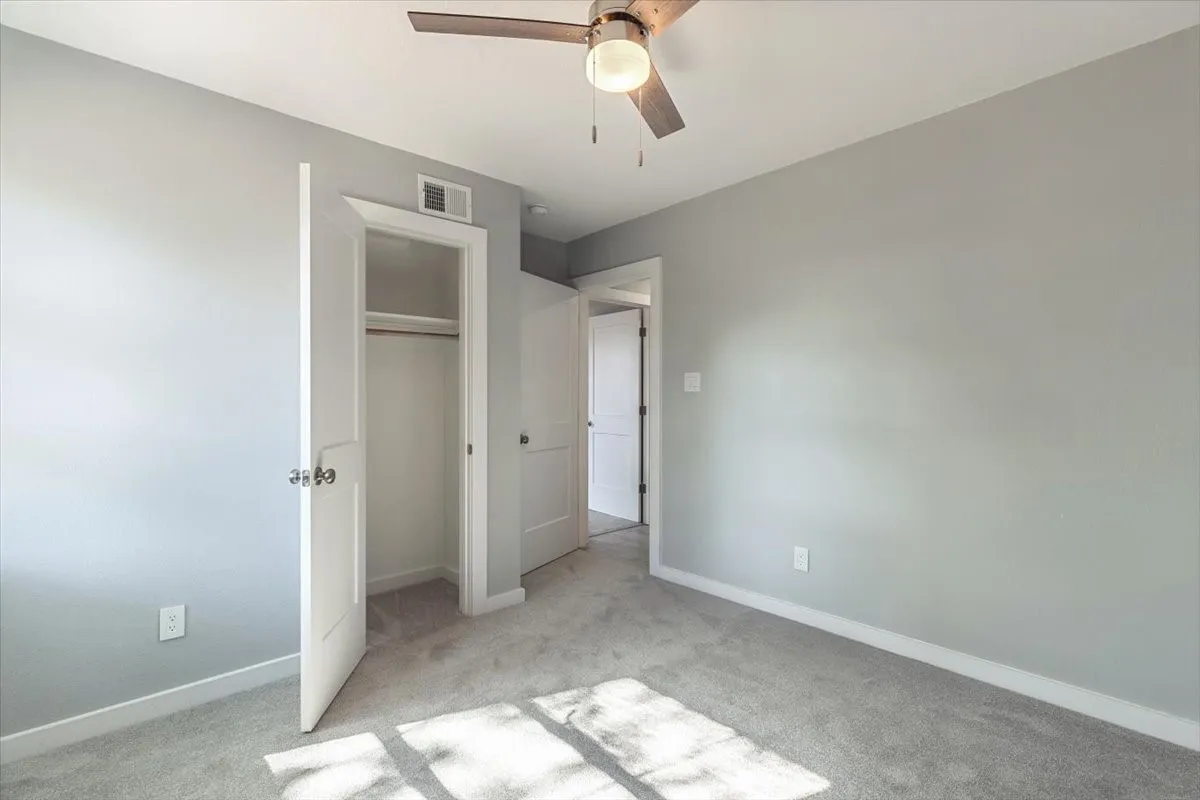 Neutral tone walls with white trim, ceiling fan with integrated lighting, soft grey carpeting, and closet with built-in rod