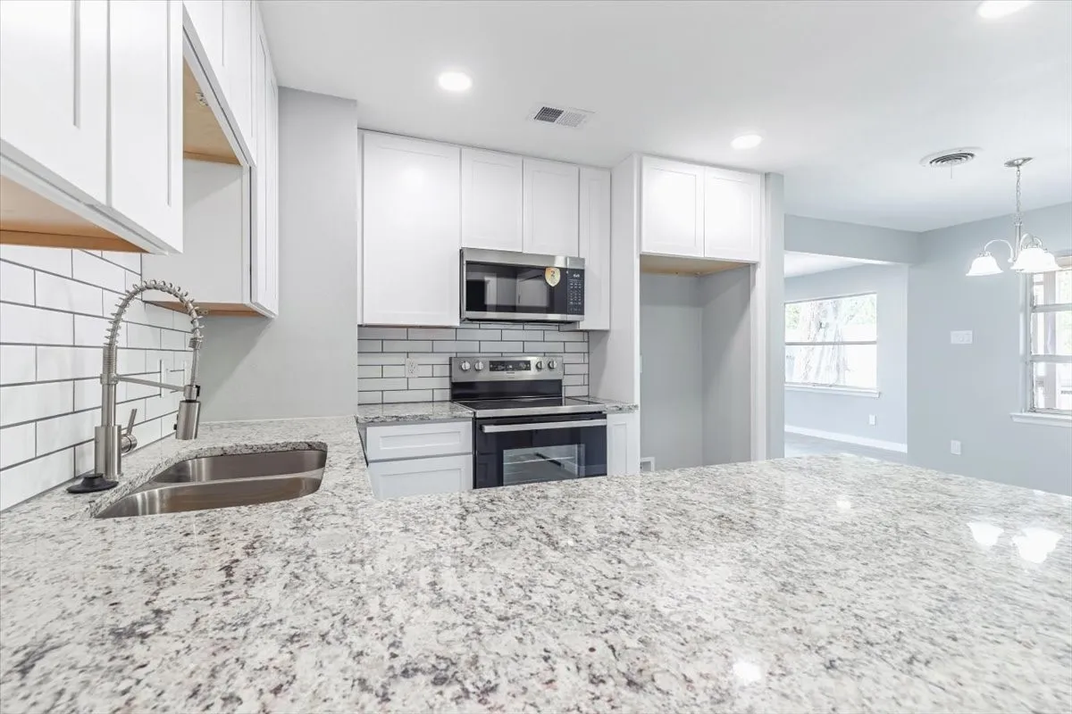 Kitchen featuring light-toned granite countertops, white cabinetry, a stainless steel sink with a gooseneck faucet, a subway tile backsplash, and stainless steel appliances