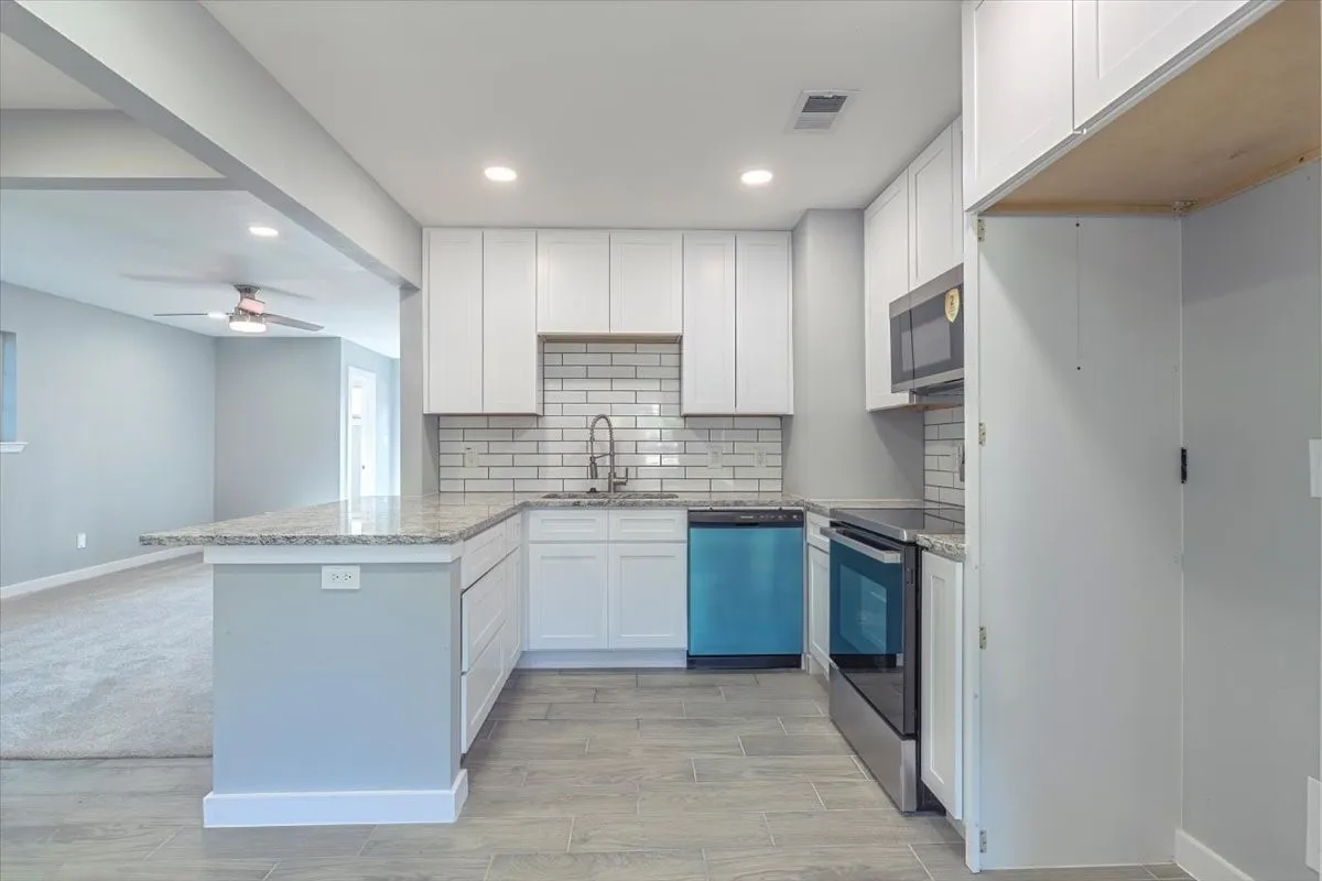 U-shaped kitchen featuring white cabinetry, light-toned countertops, a subway tile backsplash, stainless steel appliances, and wood-finish​​‌​​​​‌​​‌‌​‌‌​​​‌‌​‌​‌​‌​​​‌​​ flooring