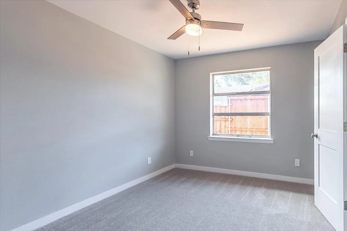 Ceiling fan with light fixture, light gray wall paint, window with white trim, and gray carpet