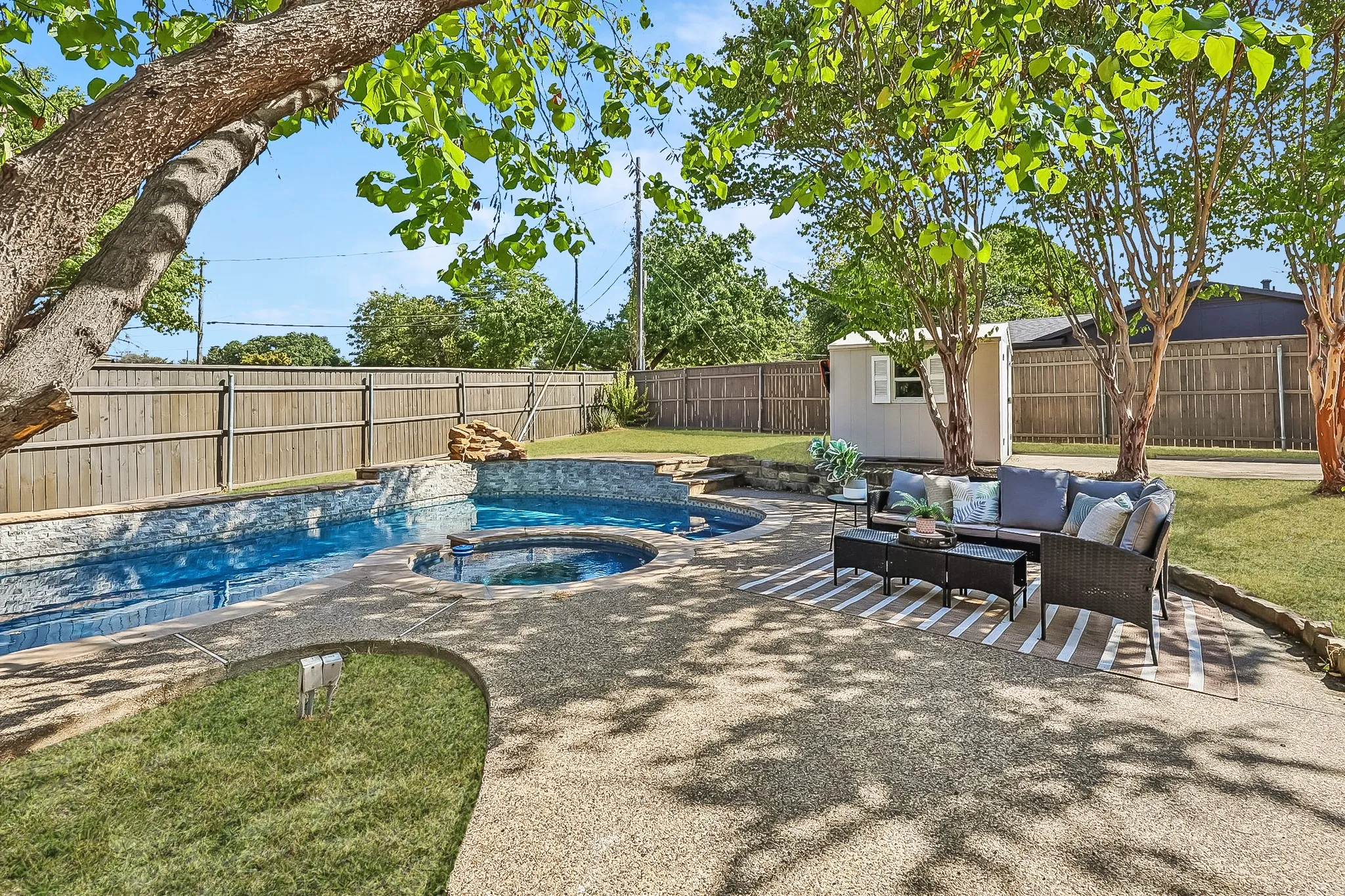 Expansive backyard featuring an in-ground swimming pool with an integrated spa, exposed aggregate concrete patio, and a utility shed