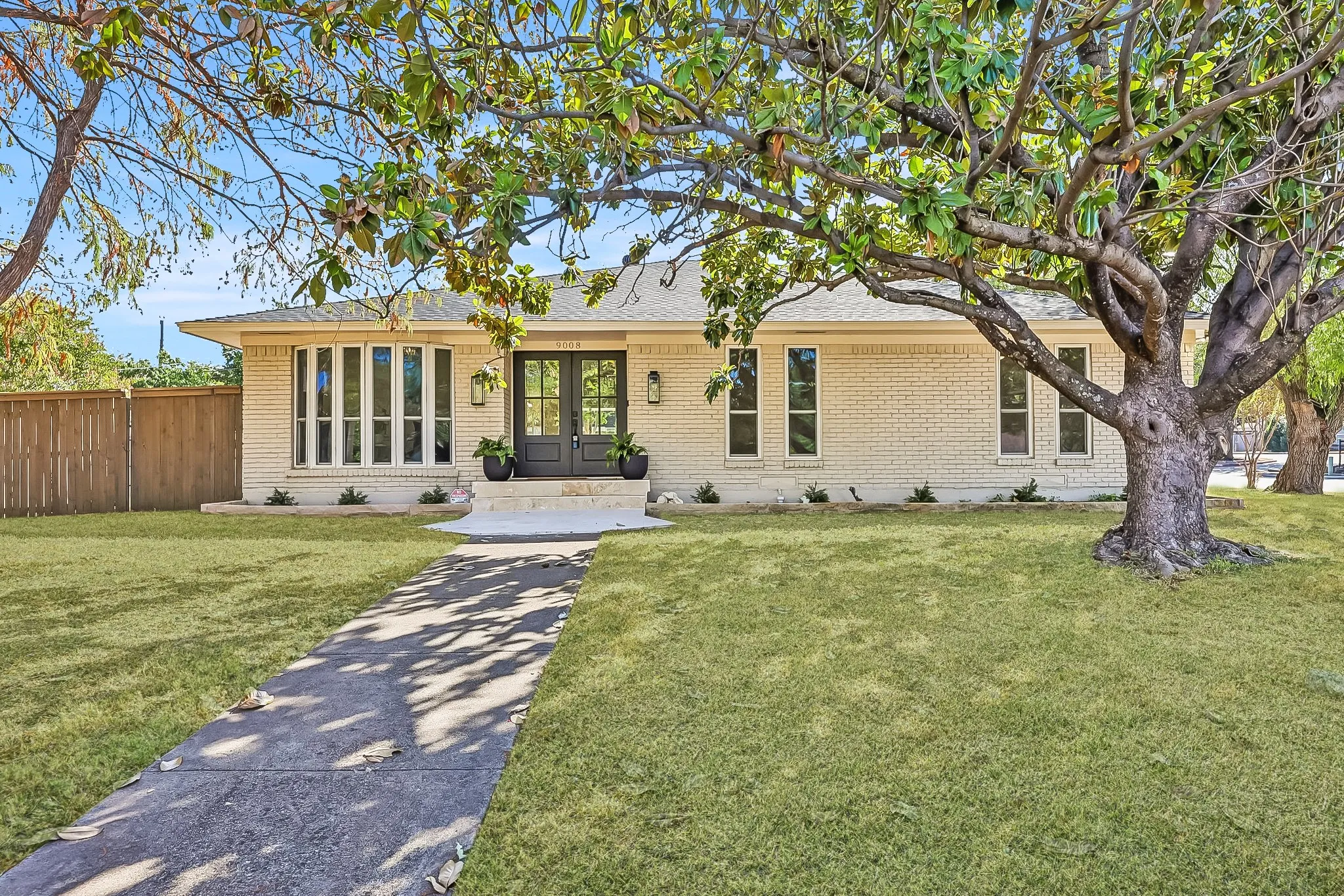 Cream brick exterior with a prominent bay window, dual entry doors, and a concrete pathway leading to the entrance