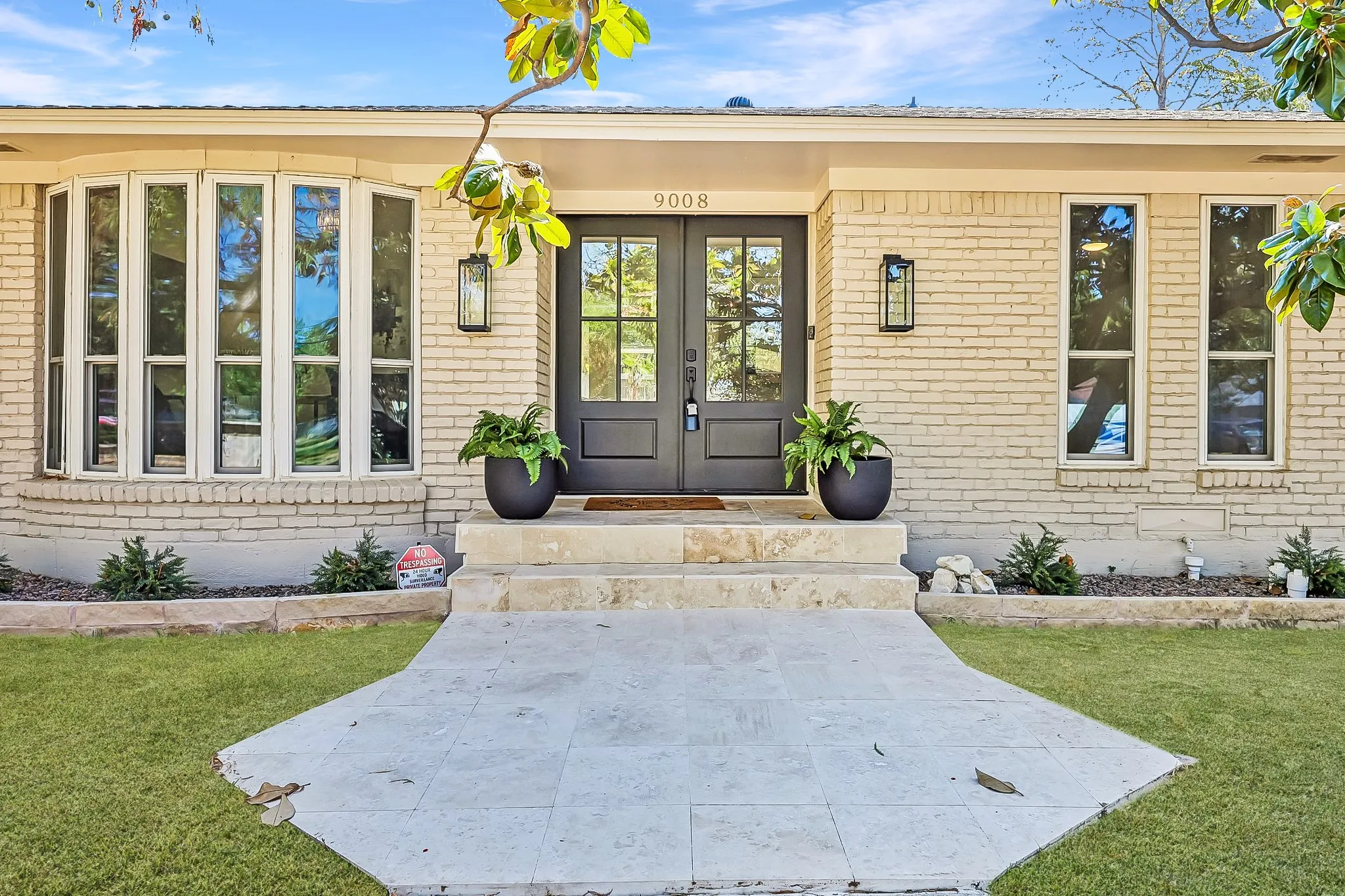 Cream brick exterior with a prominent bay window, modern double entry doors, exterior lighting fixtures, and a stone-tiled walkway leading to the entrance