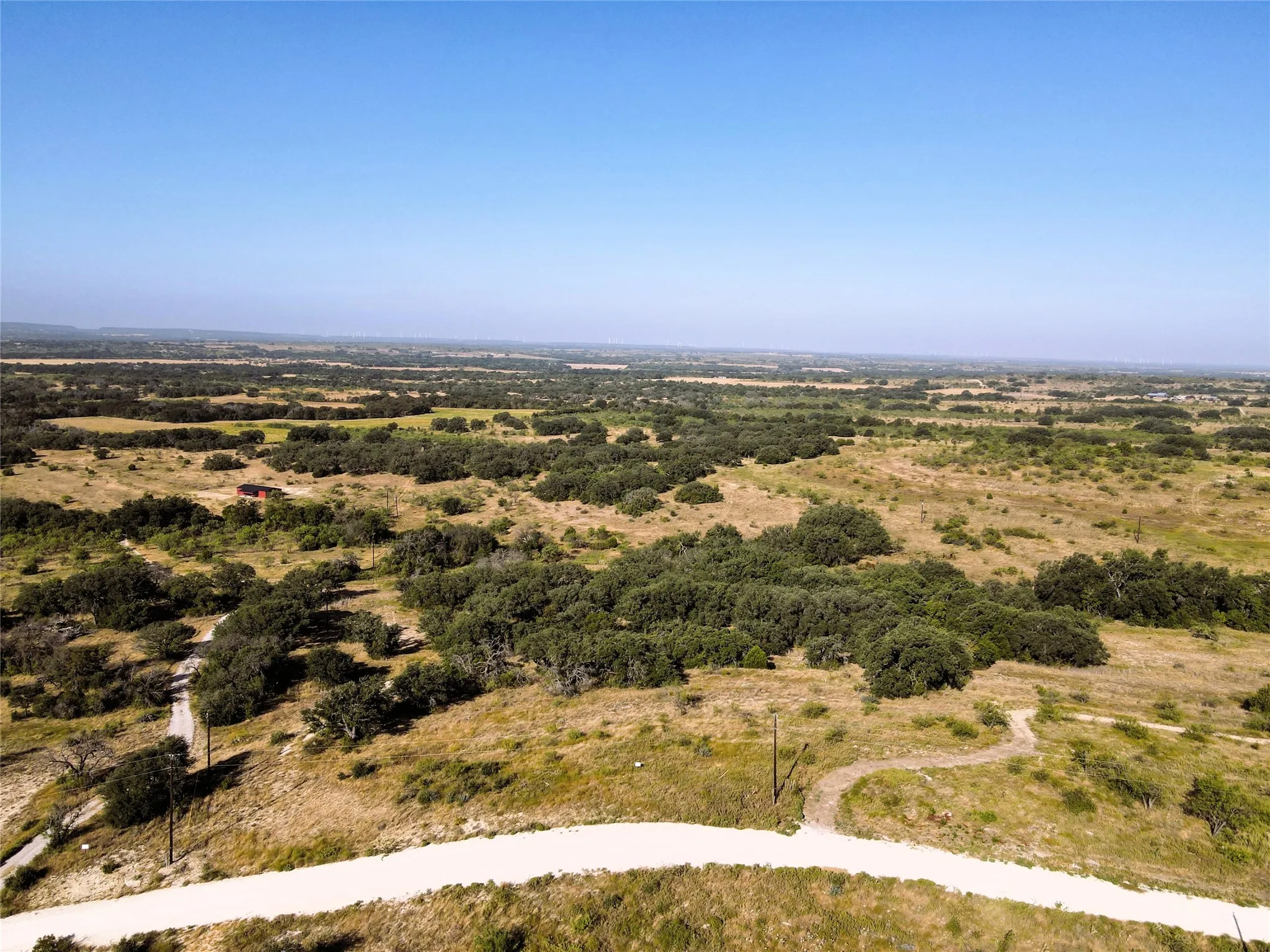 Expansive natural landscape featuring scattered mature trees, open grassy areas, and unpaved pathways