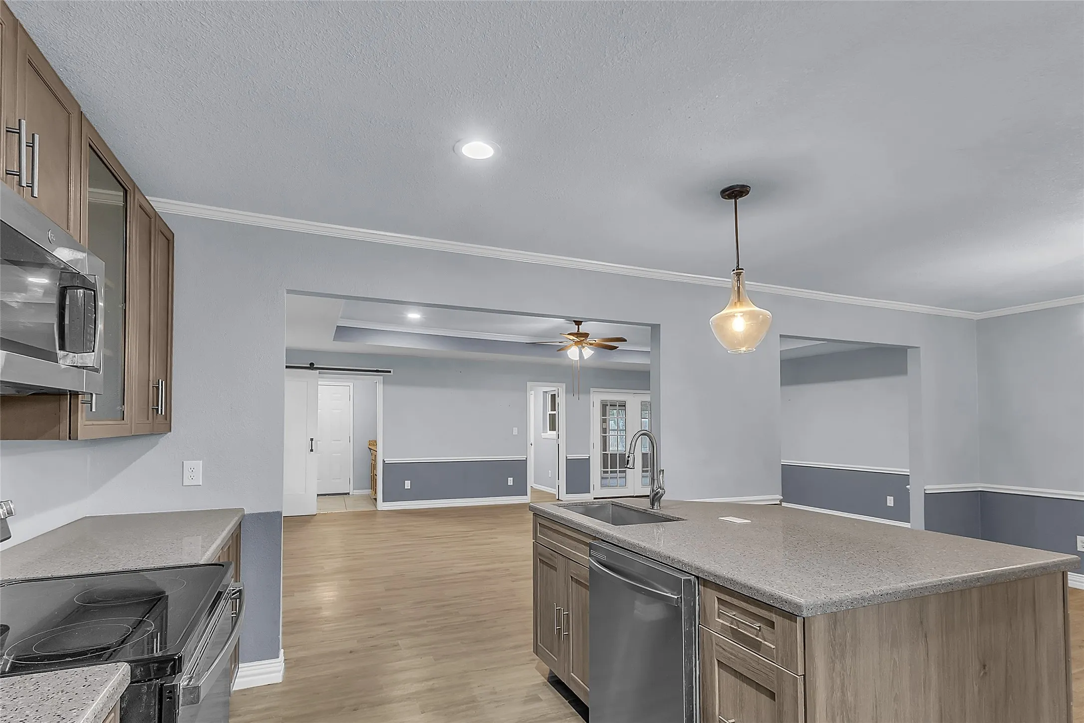 Open-plan kitchen with stainless steel appliances, quartz countertops, pendant lighting, and natural light from dual windows above the sink