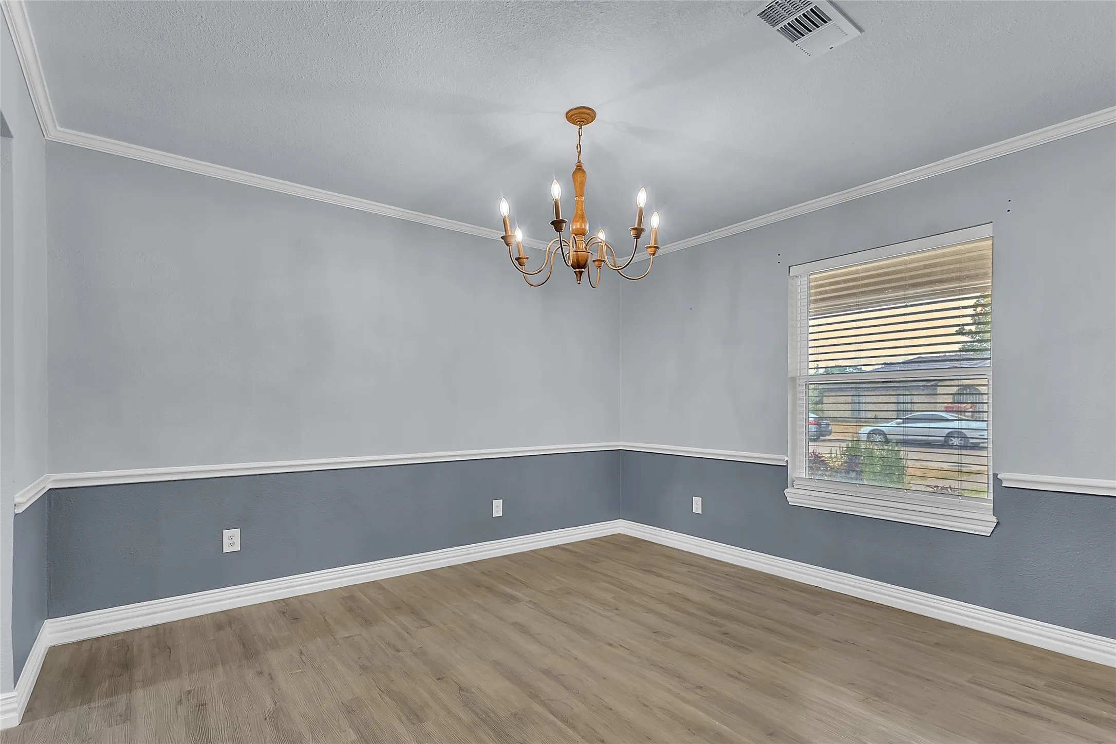 Dining room with gray walls, wood laminate flooring, a chandelier, and natural light from a window with blinds.