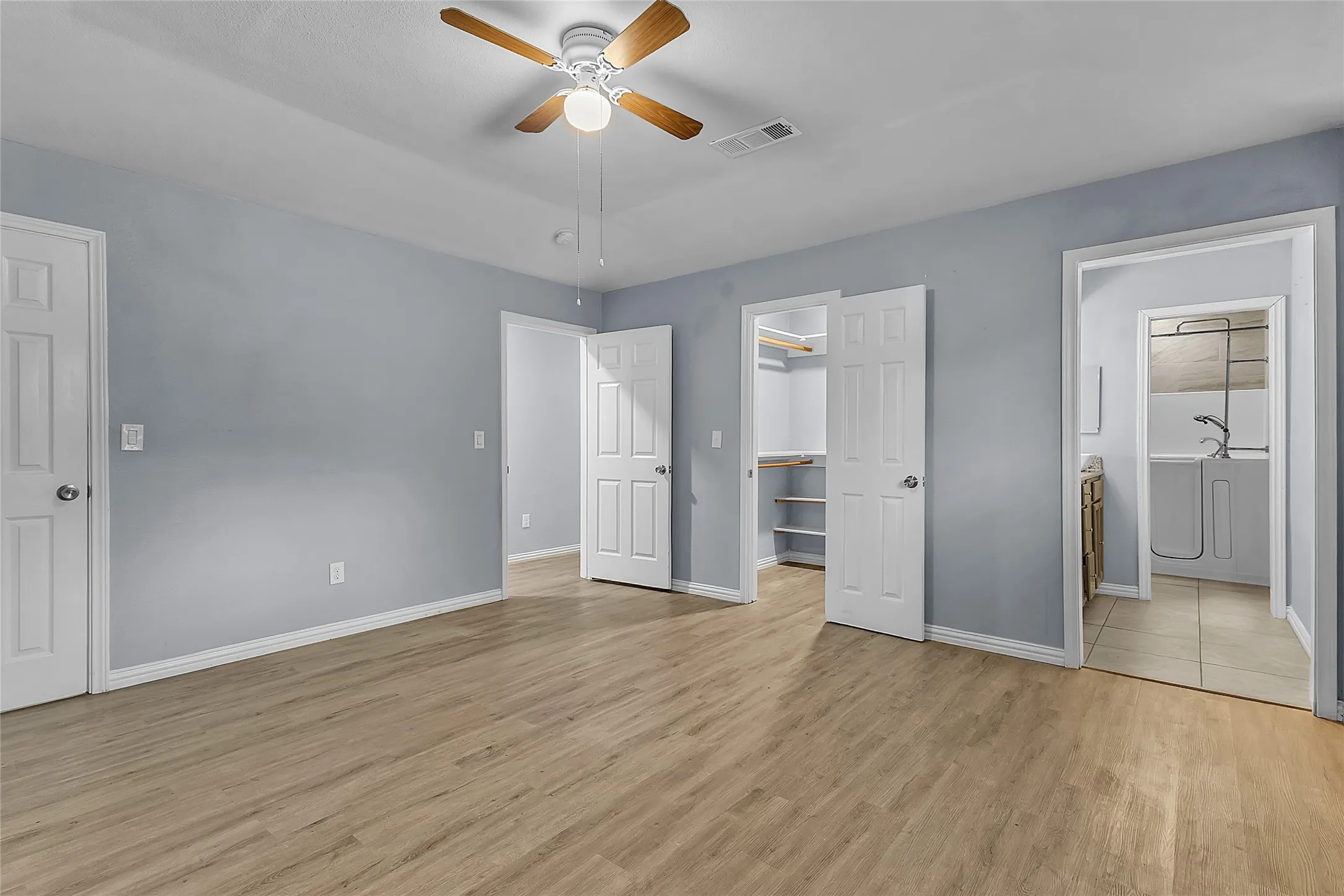 Primary bedroom with light hardwood flooring, ceiling fan, and dual closet doors leading to adjacent laundry area