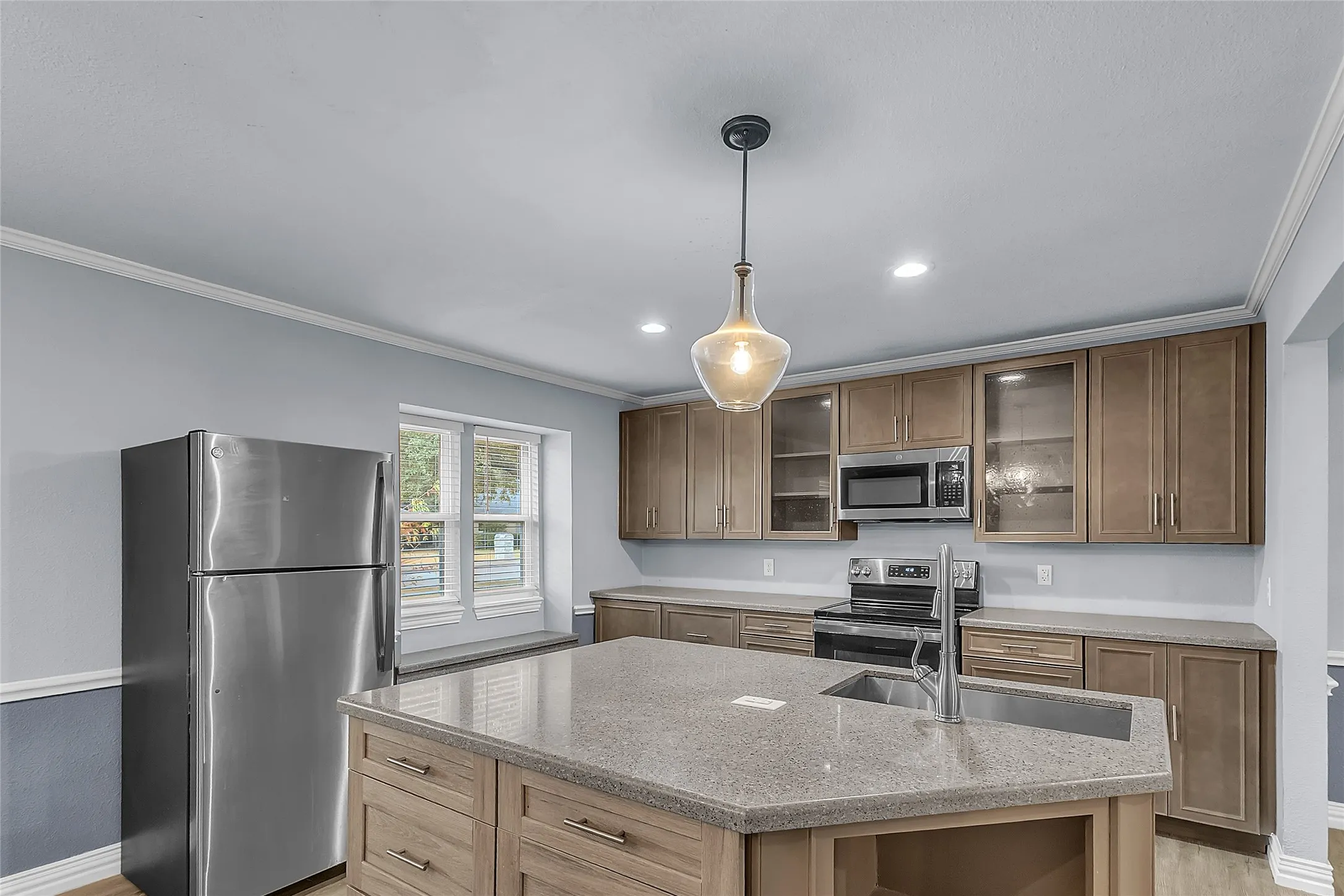 Open-plan kitchen with stainless steel appliances, recessed lighting, quartz countertops, and a central island in a light-filled layout