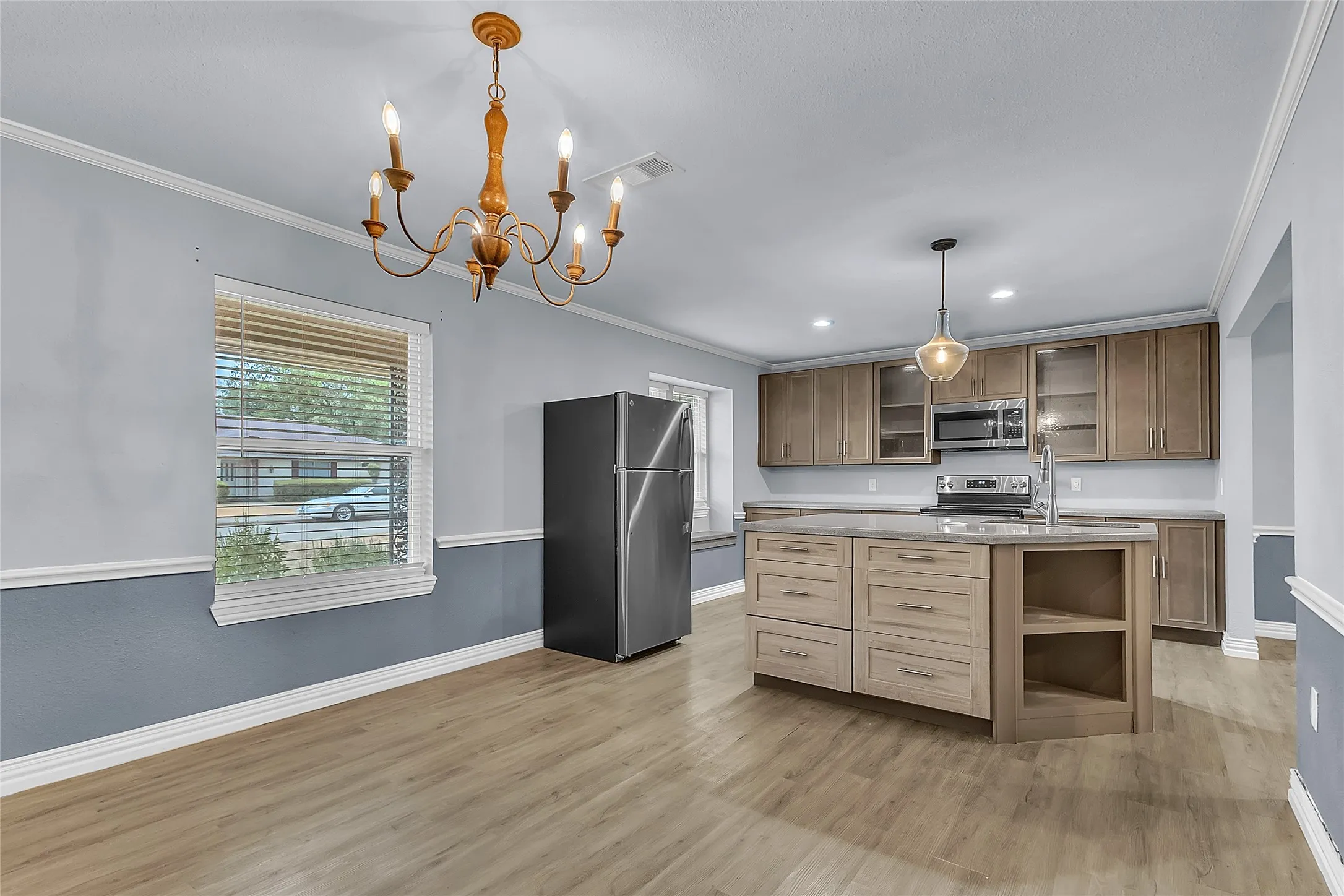 Open-plan kitchen with gray cabinets, stainless steel appliances, quartz countertops, and recessed lighting in a well-lit layout.