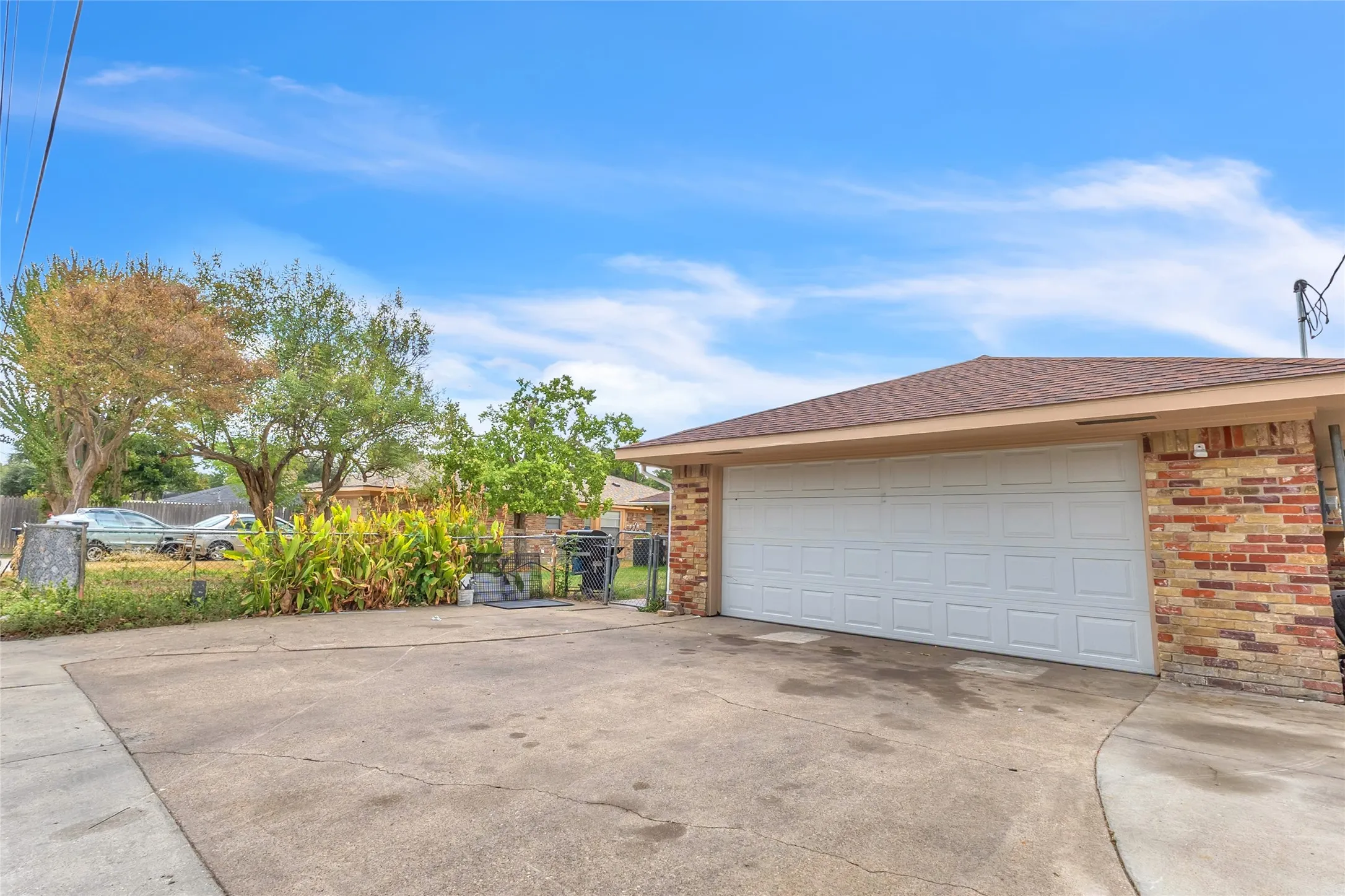 Two-car garage with a concrete driveway, stone brick exterior, and side yard greenery visible in the background under a clear blue sky