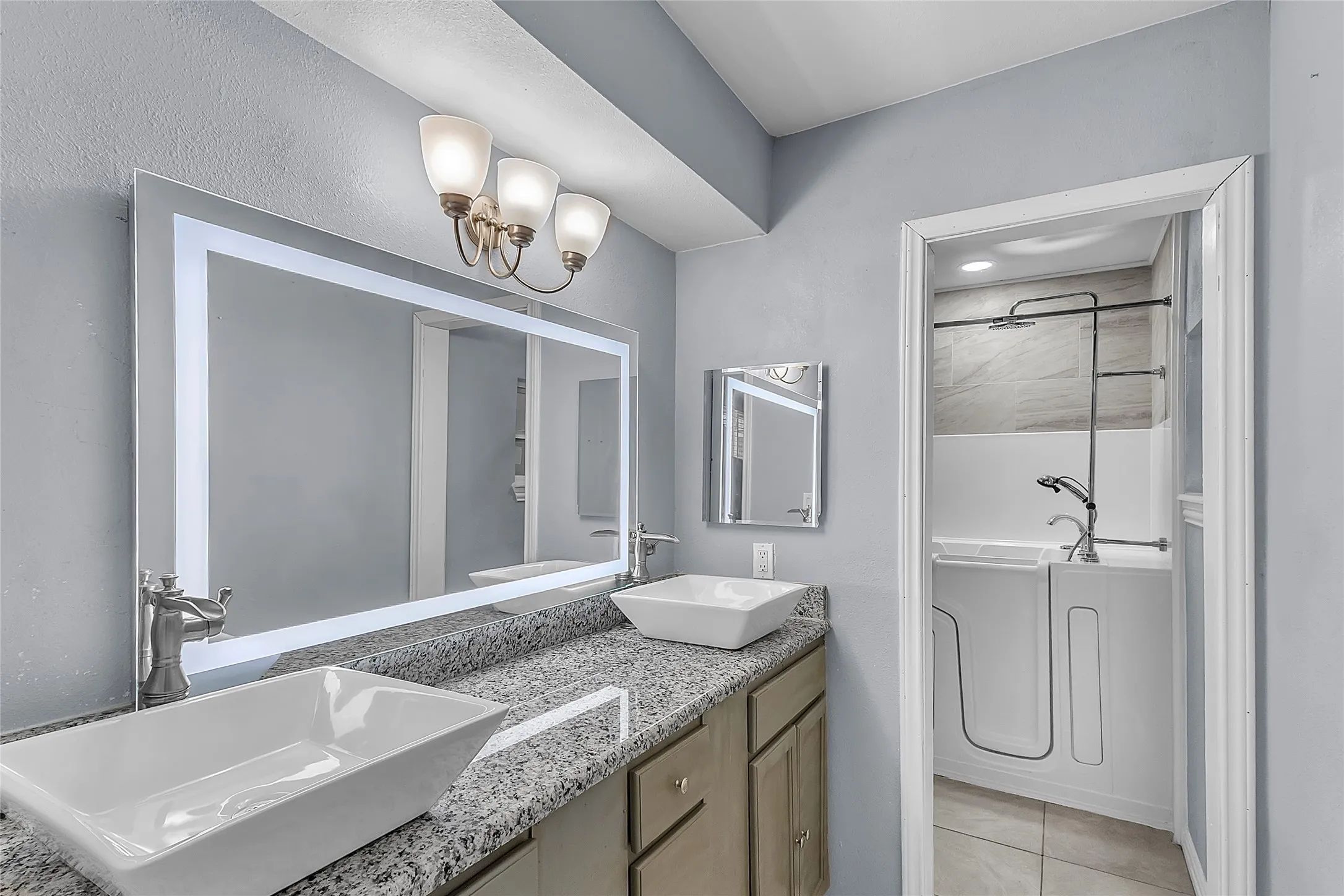 Bathroom with dual vessel sinks, granite countertops, modern lighting, and a separate laundry area with porcelain tile flooring and a sleek mirrored layout