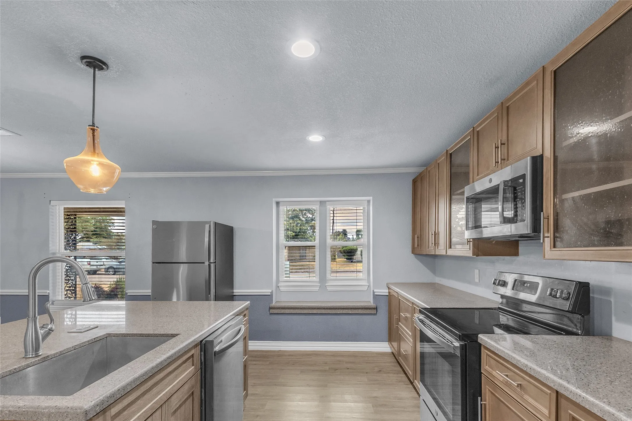 Open-plan kitchen with quartz countertops, stainless steel appliances, recessed lighting, and large window providing natural light.