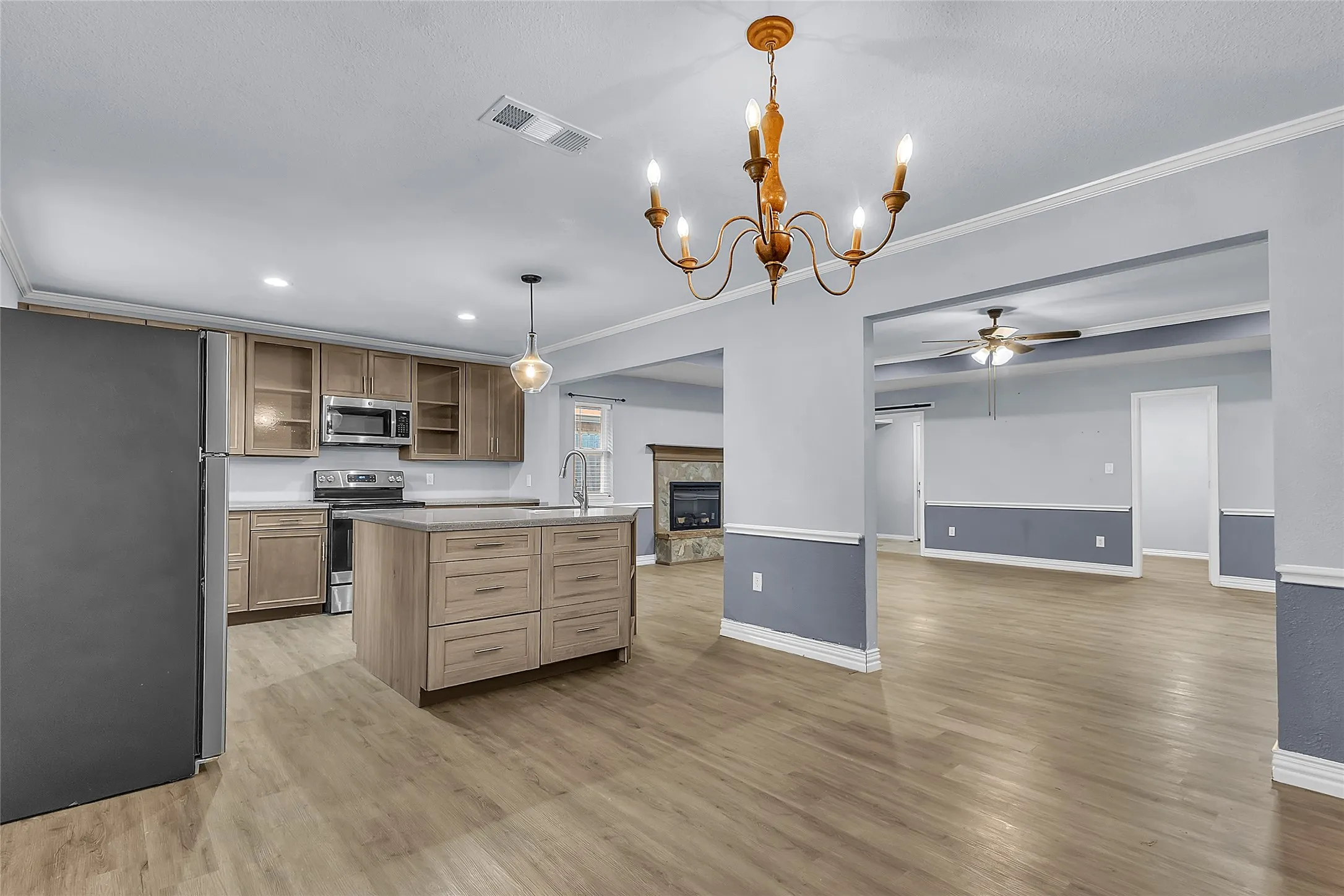 Open-plan kitchen with stainless steel appliances, quartz countertops, hardwood flooring, and recessed lighting under a chandelier