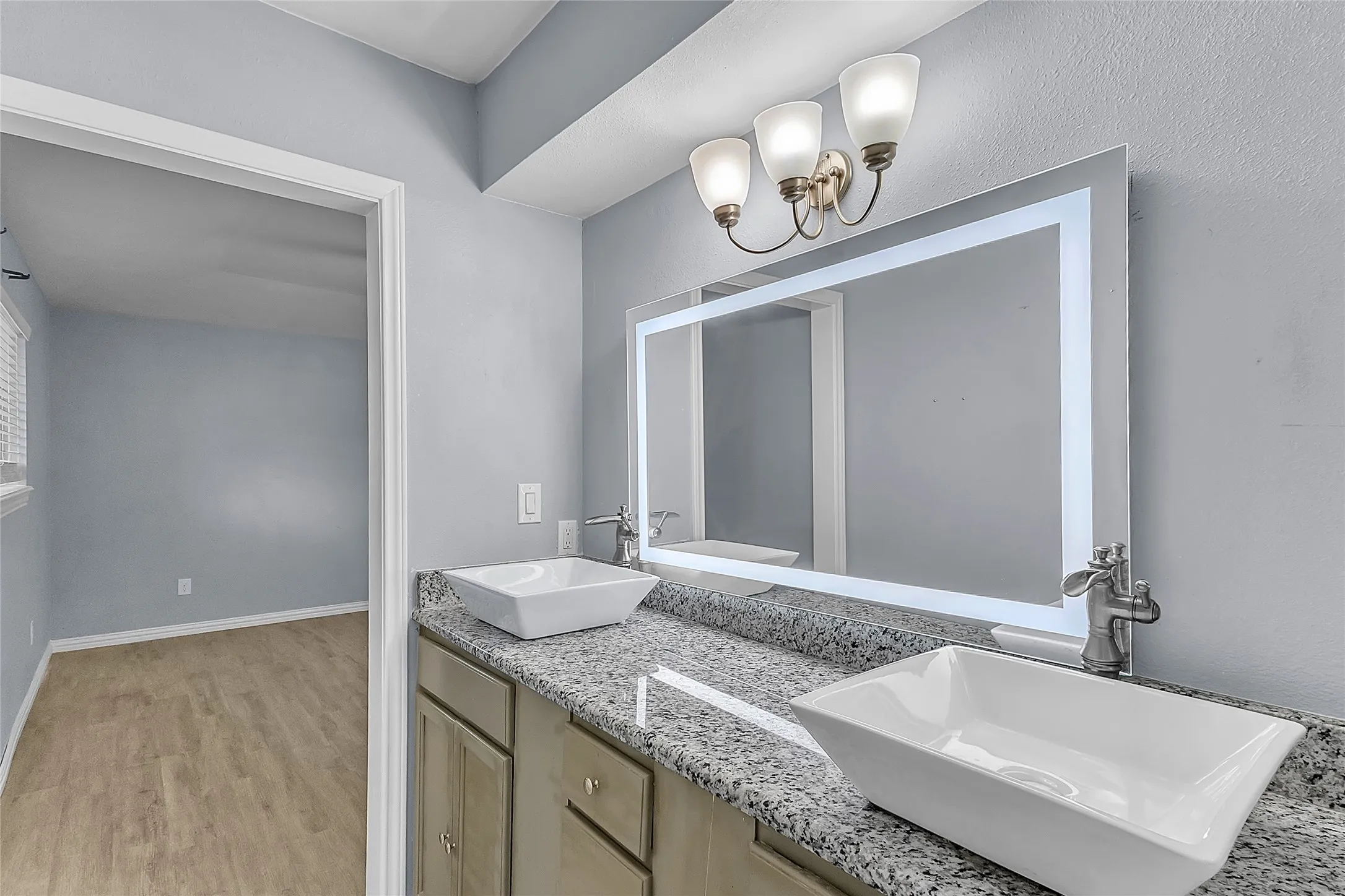 Bathroom with dual vessel sinks, granite countertop, and modern light fixtures; natural light enhances the serene color palette and open layout.