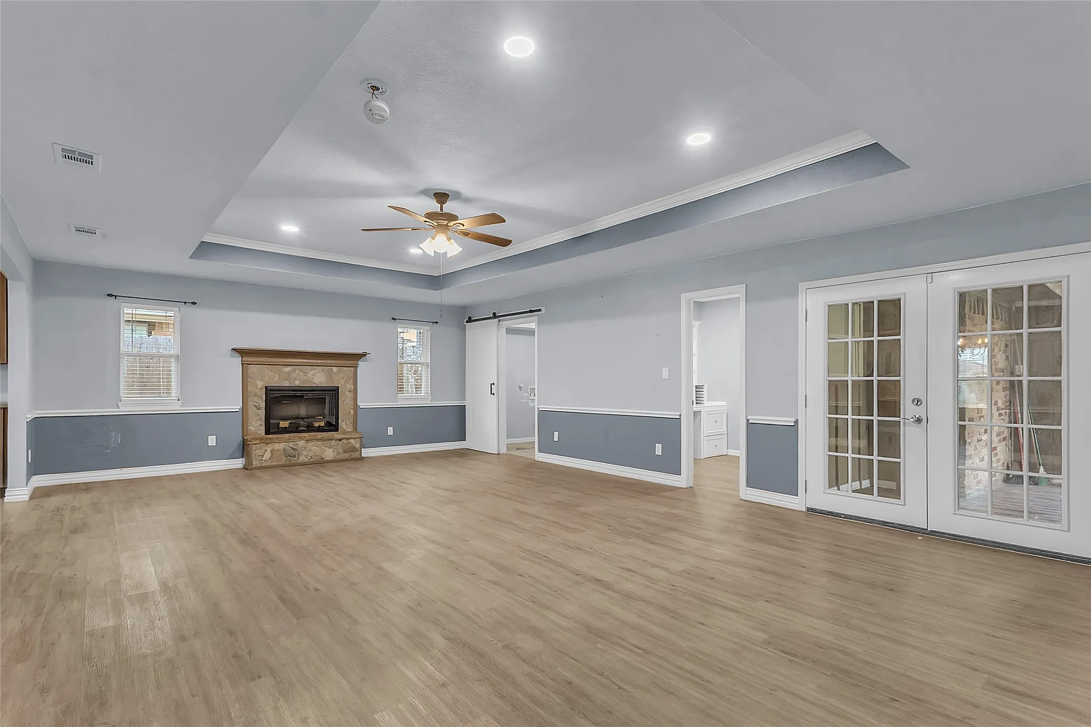 Living room with vaulted ceiling, hardwood flooring, stone fireplace, and access to a covered patio through French doors.