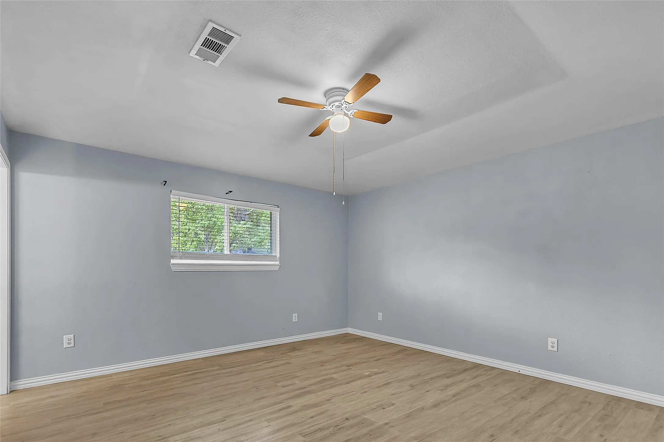 Primary bedroom with light-colored walls, hardwood flooring, ceiling fan, and a window providing natural light.