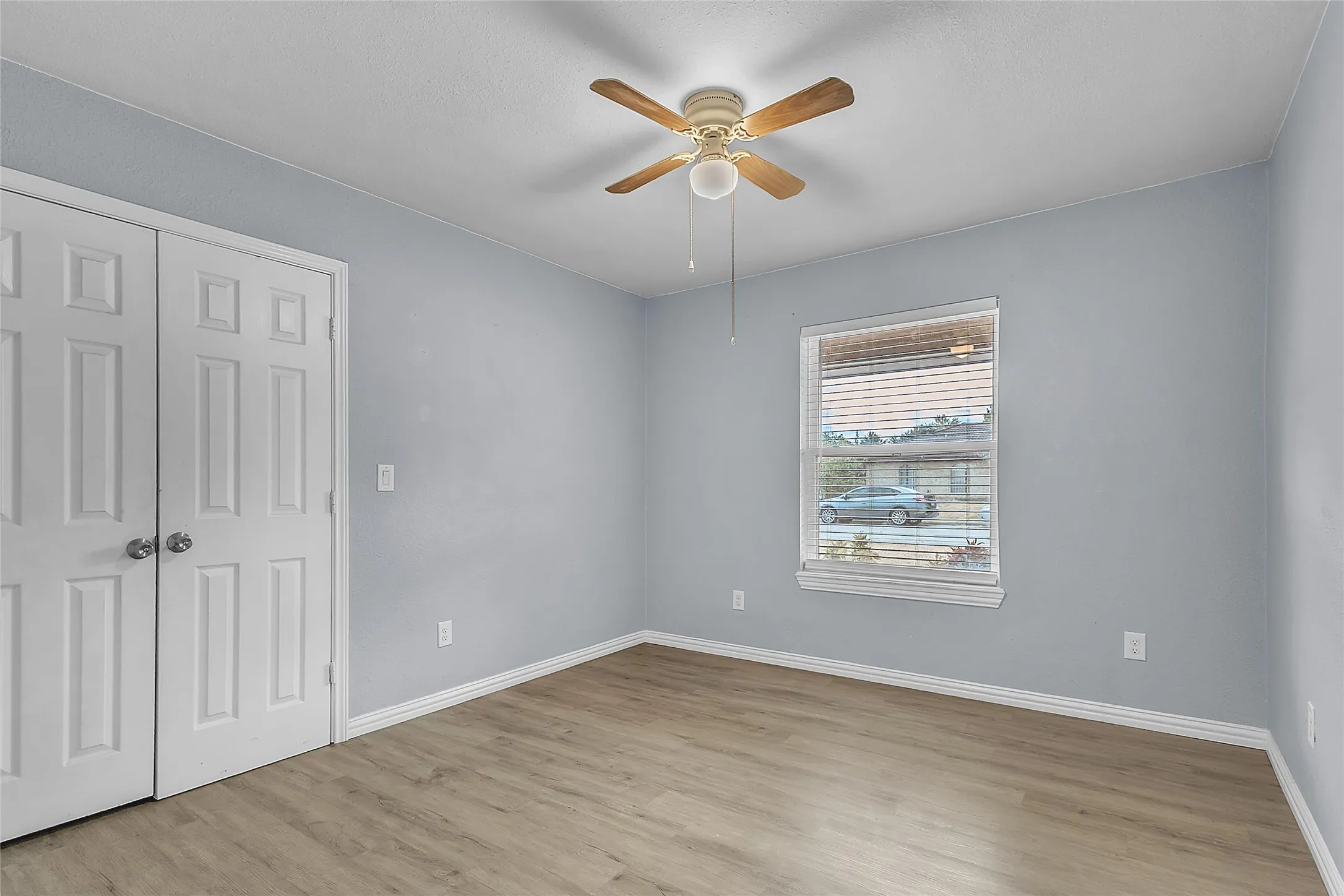 Bedroom with light-colored walls, laminate flooring, ceiling fan, and natural light from a window with blinds. Double closet doors enhance storage options.