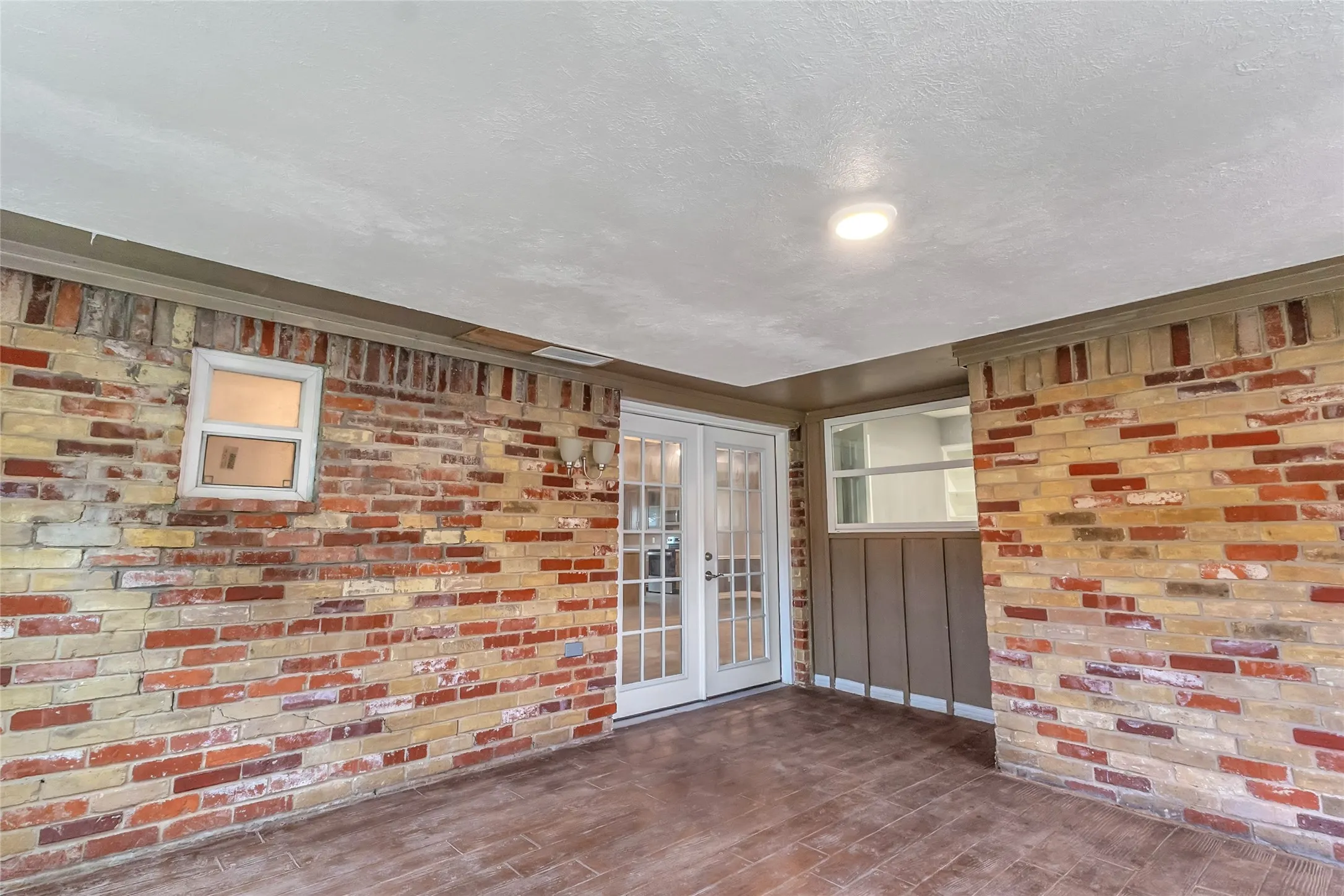 Covered back patio with brick walls, oversized windows, and recessed lighting on a smooth ceiling.