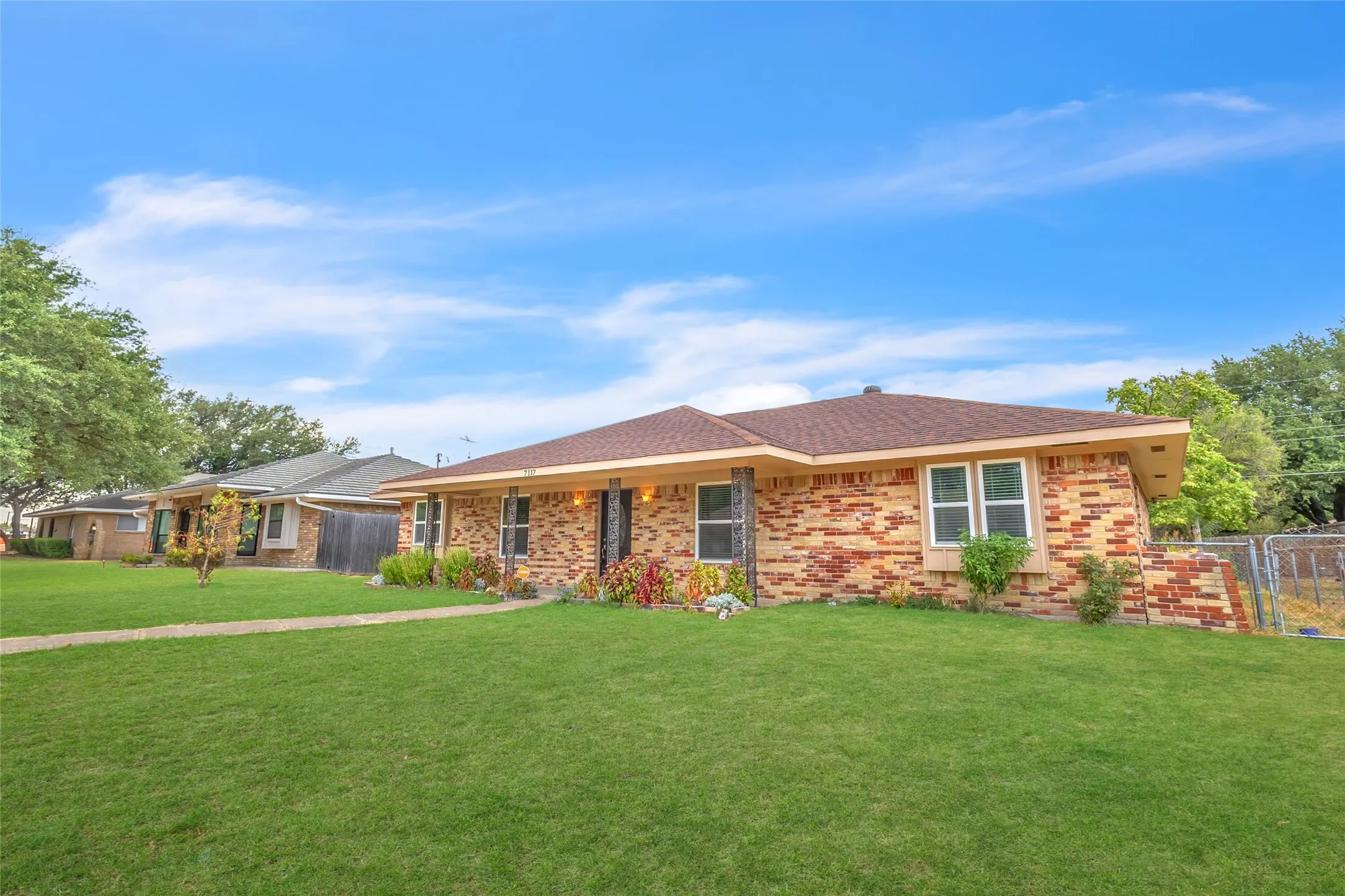 Brick exterior home with a gable roof, landscaped front yard, and adjacent single-story residences under a clear blue sky.