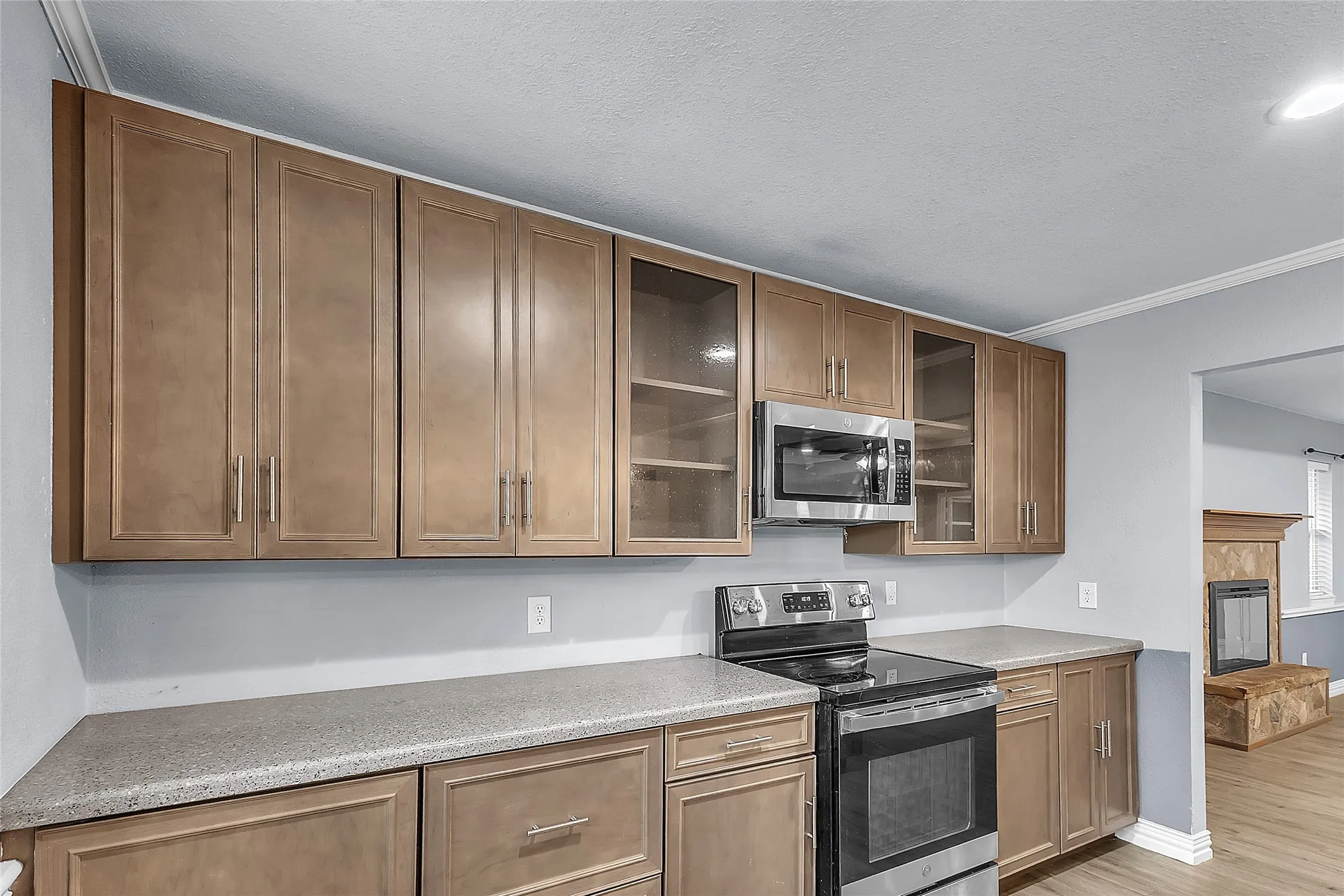 Open-plan kitchen with beige cabinetry, stainless steel appliances, and quartz countertops, illuminated by recessed lighting and showcasing a clean layout