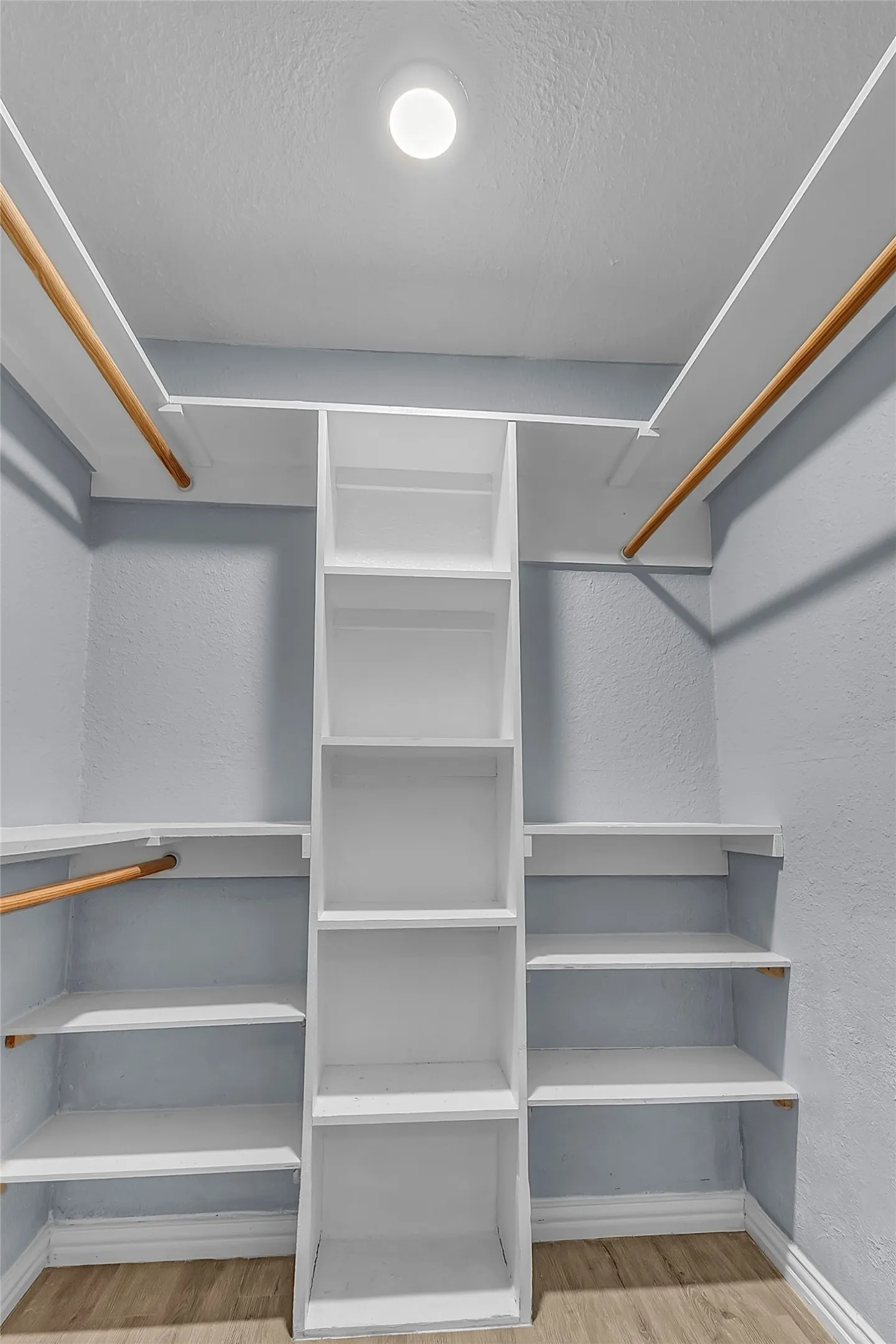Walk-in closet with built-in shelving, dual hanging rods, and recessed lighting in a light gray finish.