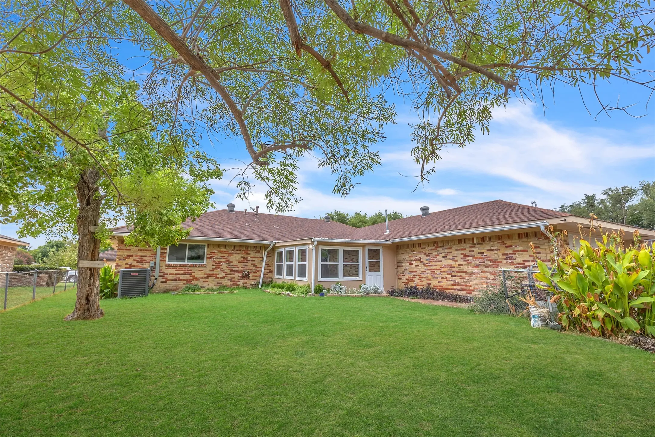 Backyard view with brick exterior, well-maintained lawn, shade from mature trees, and outdoor storage area.