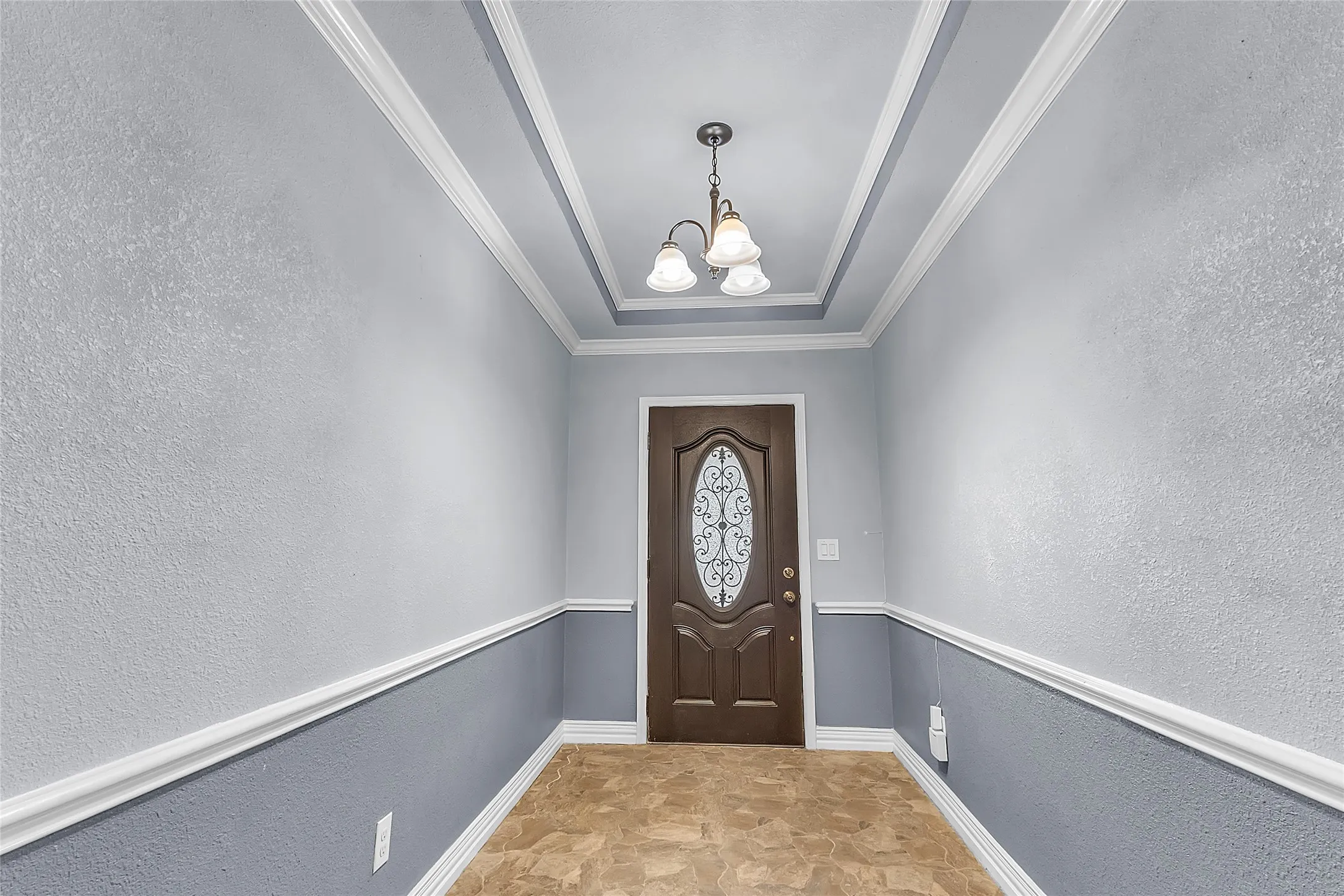 Entryway with a decorative front door, LVP flooring, crown molding, and three pendant lights accentuating the high ceiling and welcoming layout
