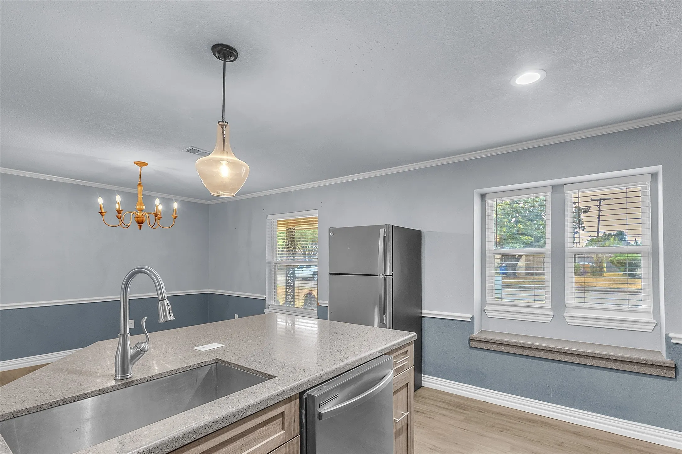 Open-plan kitchen with stainless steel appliances, quartz countertops, pendant lighting, and natural light from dual windows above the sink
