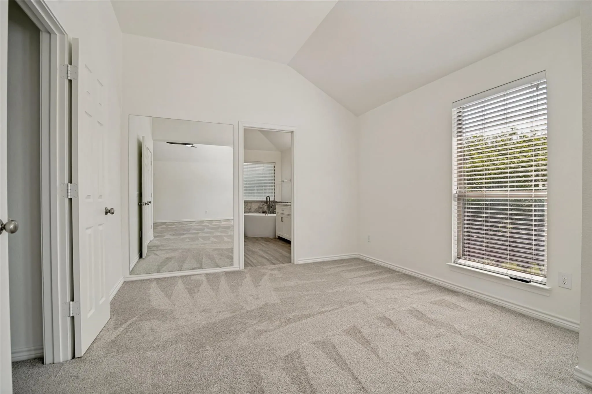 Vaulted ceiling, neutral tone carpeting, window with blinds, interior door, and mirrored closet doors