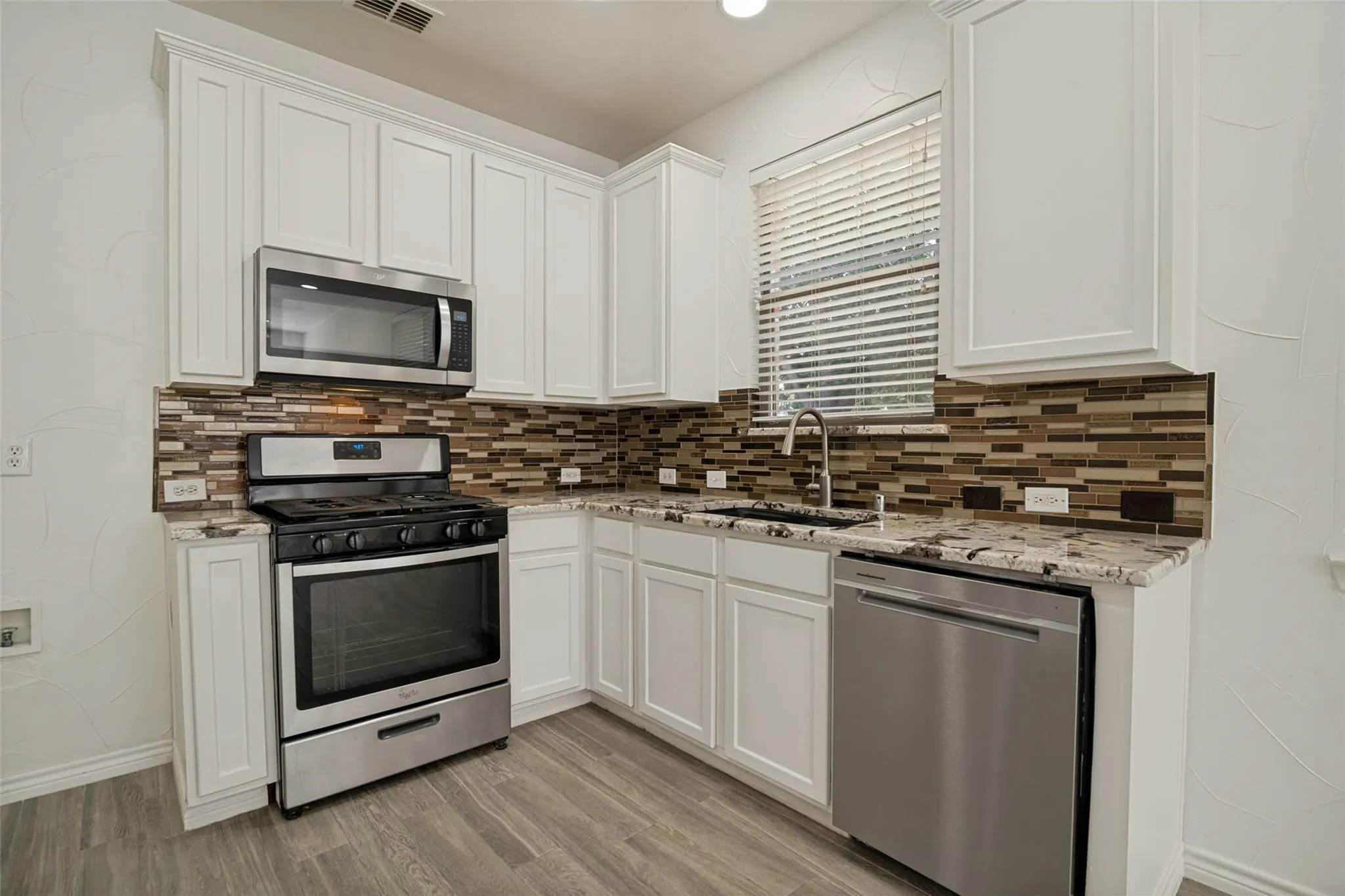 Kitchen featuring white cabinetry, stainless steel appliances, granite-style countertops, mosaic tile backsplash, and wood-finish flooring