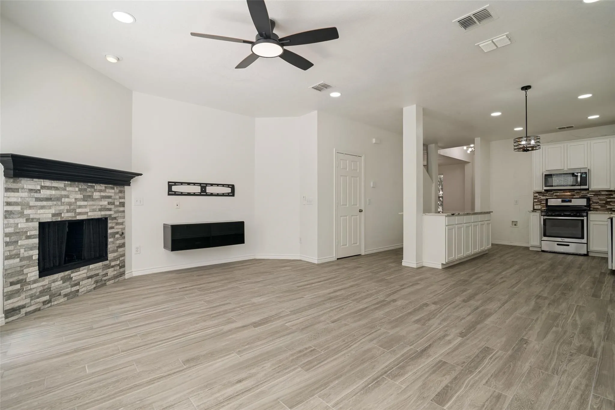 Spacious living area featuring wood-finish tile flooring, a fireplace with a stone surround and dark wood mantel, and a ceiling fan