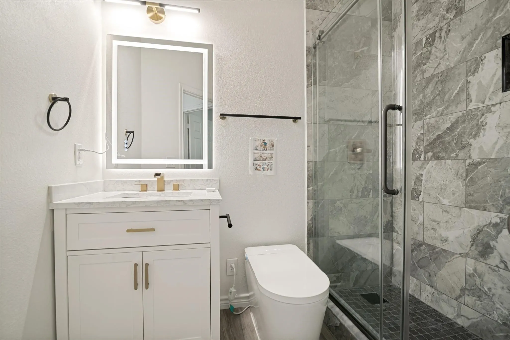Walk-in shower with tiled walls and glass enclosure, floating vanity with a stone countertop, illuminated mirror, and modern toilet