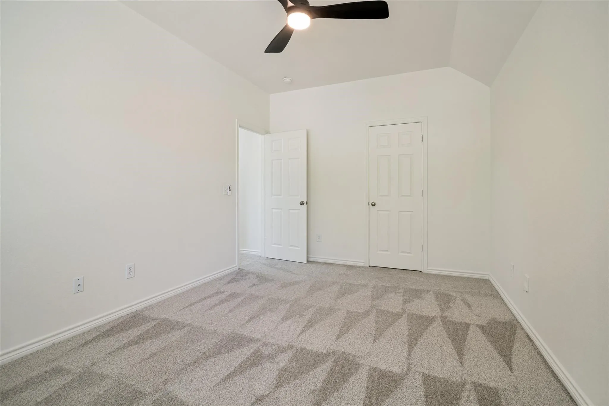 Vaulted ceiling, ceiling fan, neutral paint palette, paneled doors, and patterned carpet