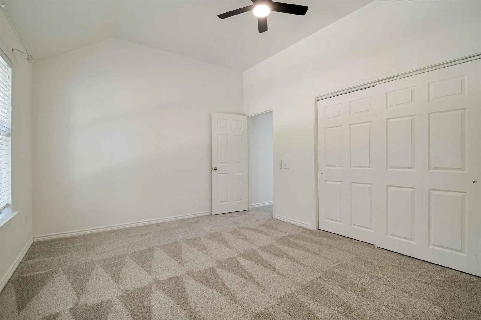 Vaulted ceiling with a ceiling fan, patterned carpet flooring, sliding closet doors, and window blinds