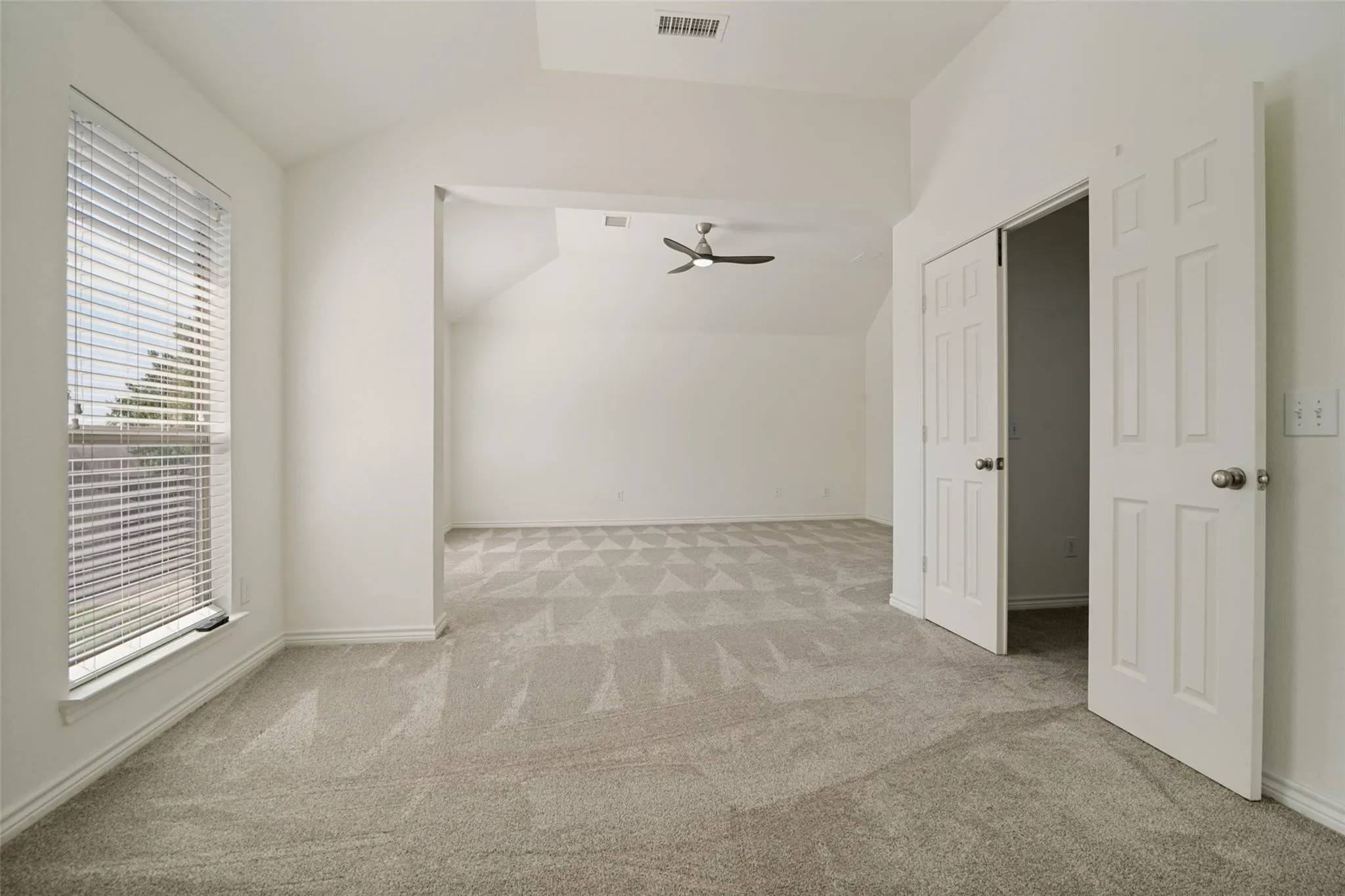 Spacious interior featuring a large window with blinds, light-toned patterned carpeting, and white paneled doors