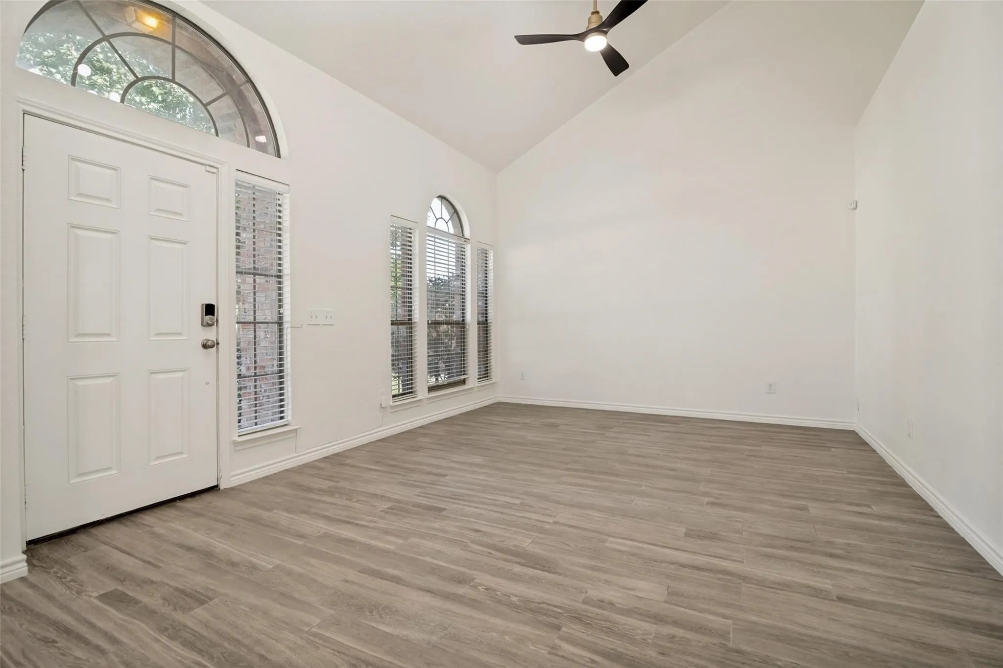 Vaulted ceiling with a black ceiling fan, wood-finish flooring, white panel door, and arched transom windows